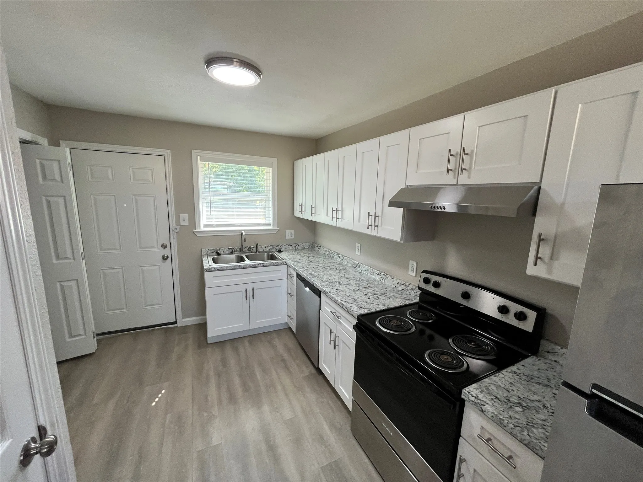 Kitchen featuring white cabinetry, light-toned countertops, wood-finish flooring, a stainless steel range hood, and a dual-basin sink