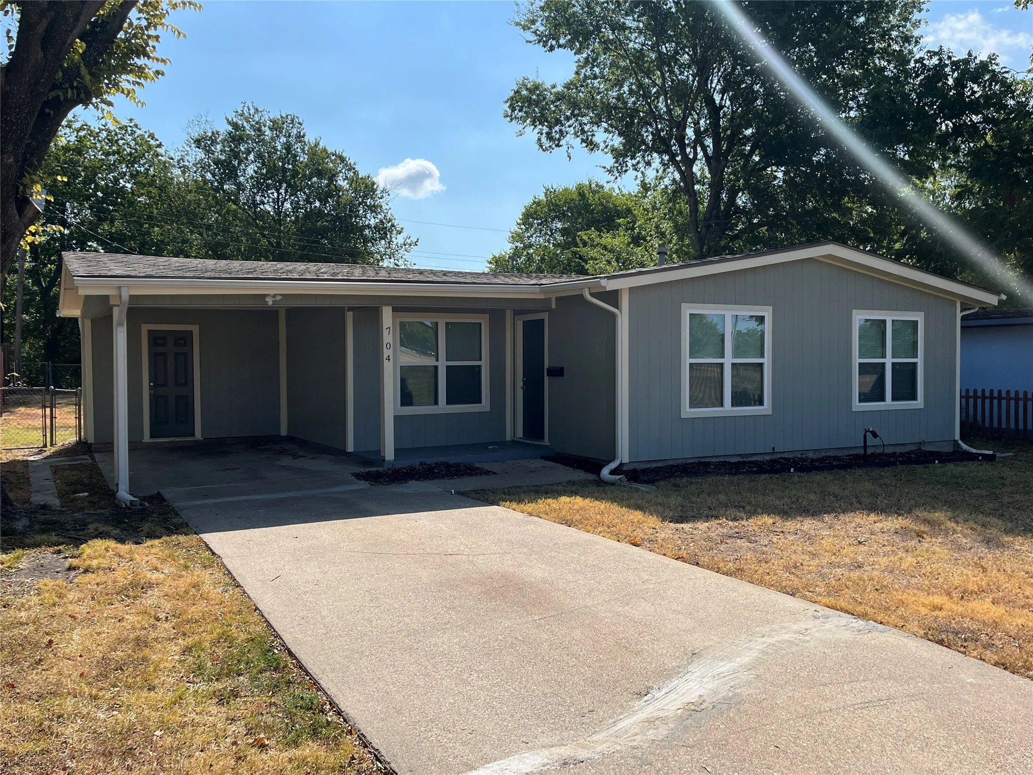 Single-story residence featuring light gray siding, white window trim, and a covered carport