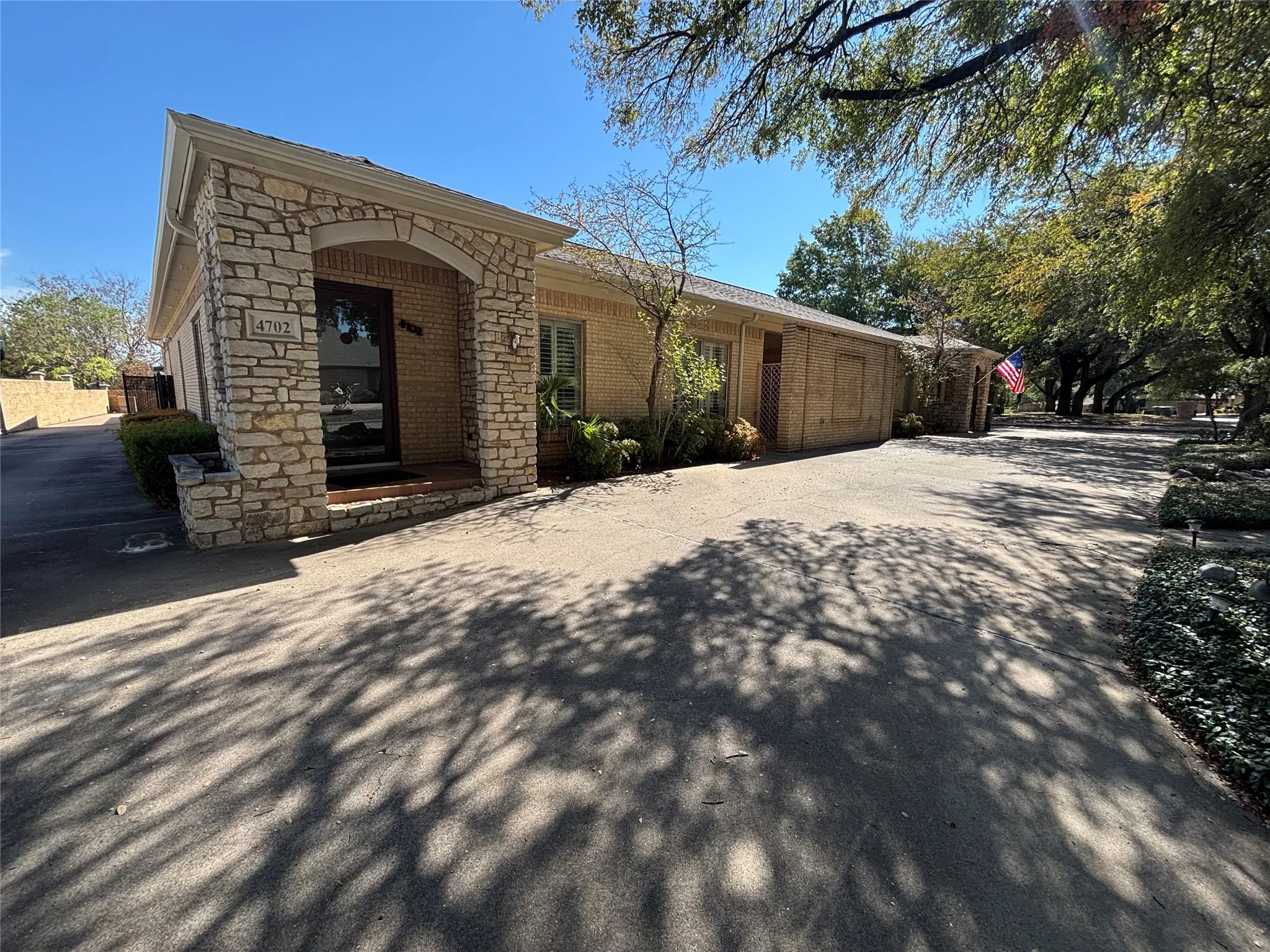 Stone-clad arched entryway with a solid door, brick exterior, and mature tree landscaping