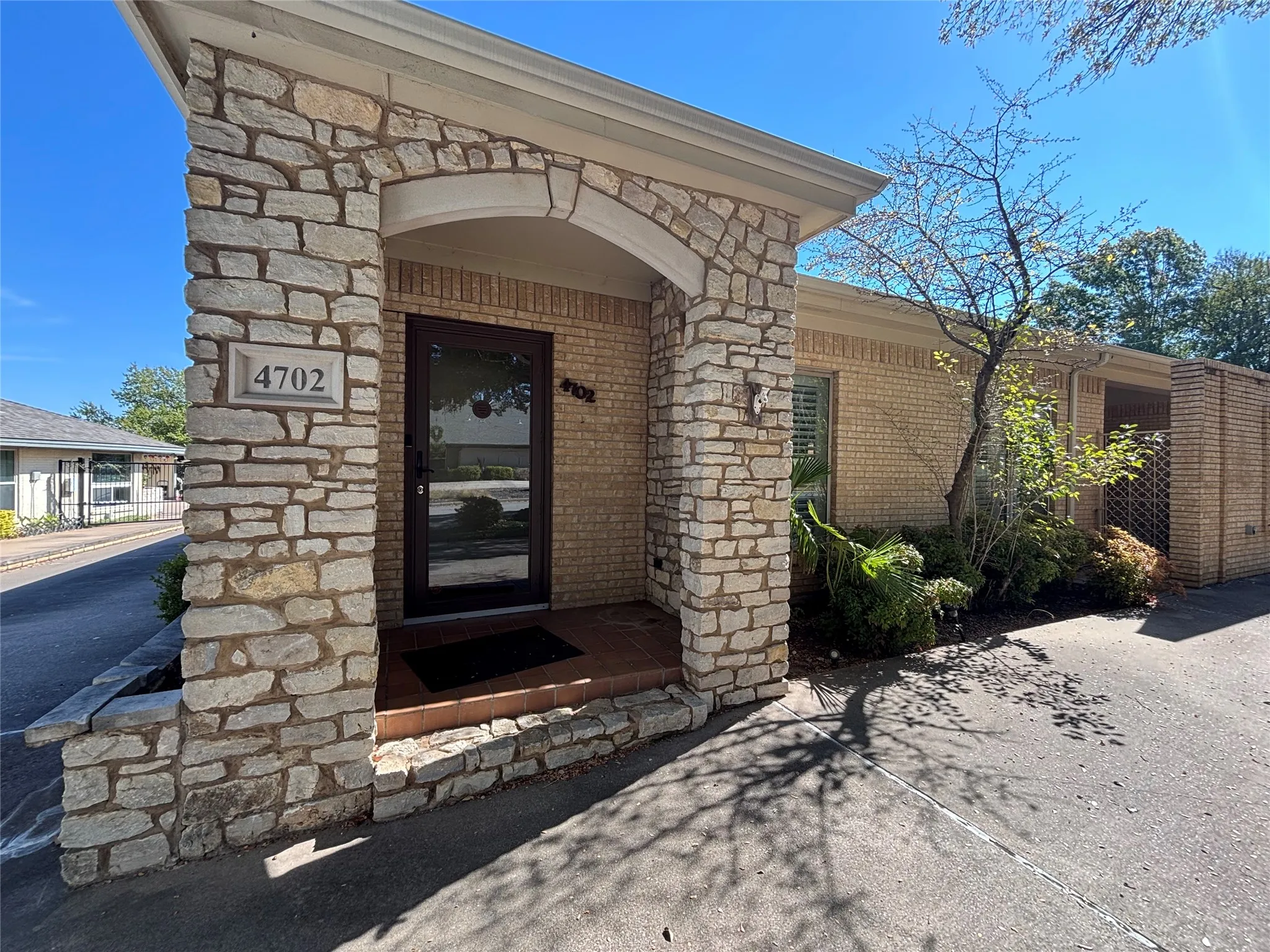 Stone-clad front entry with an arched portico, brick exterior, dark-framed storm door, and established landscaping