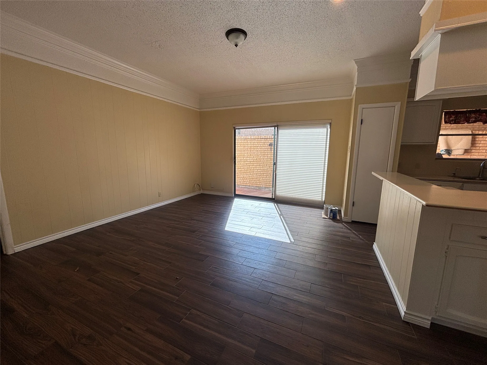 Wood-finish flooring, crown molding, sliding glass door, white kitchen cabinetry, and a kitchen island with a light-toned countertop