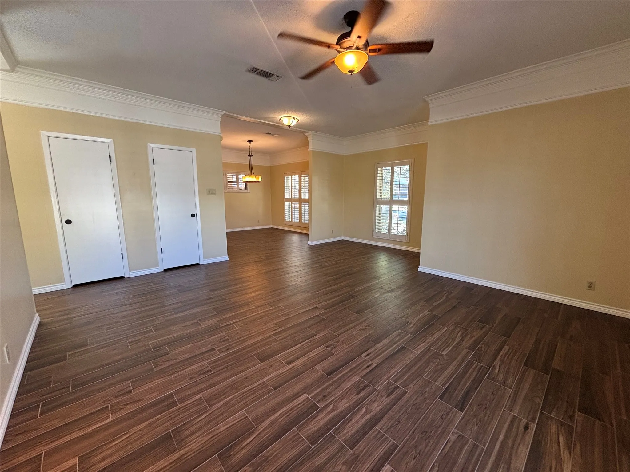 Spacious interior featuring wood-look tile flooring, crown molding, and plantation shutters