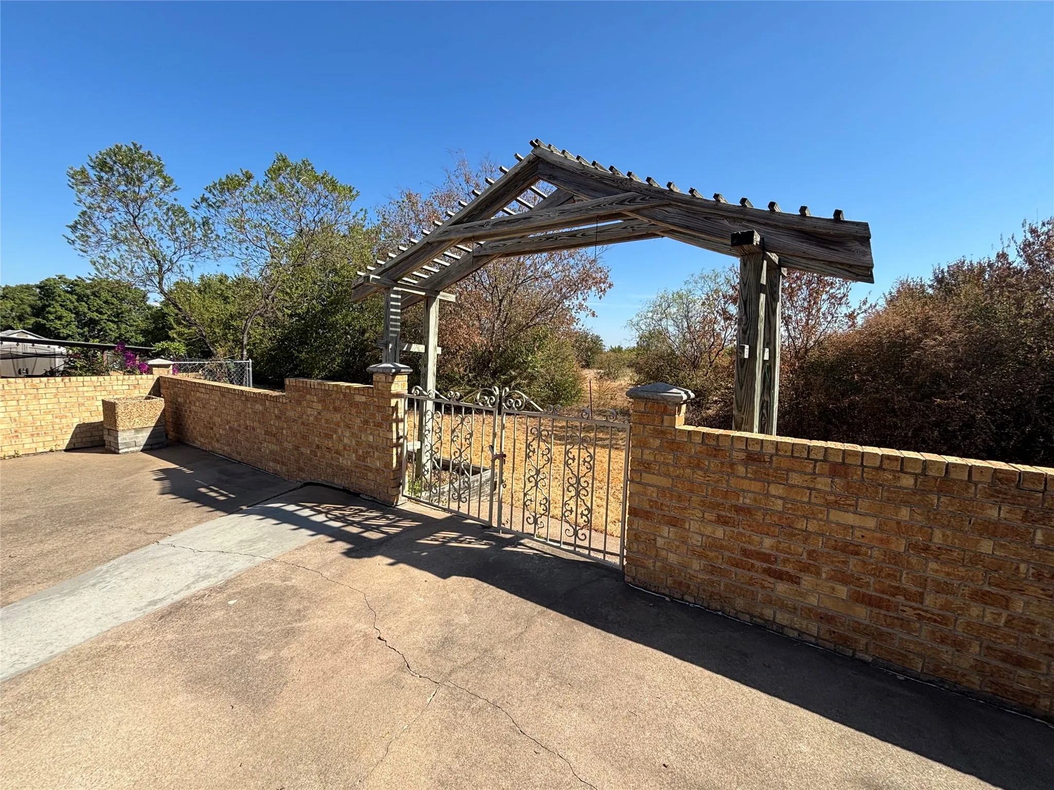 Brick wall with capstone detail, wrought iron gate, and a wood pergola entry