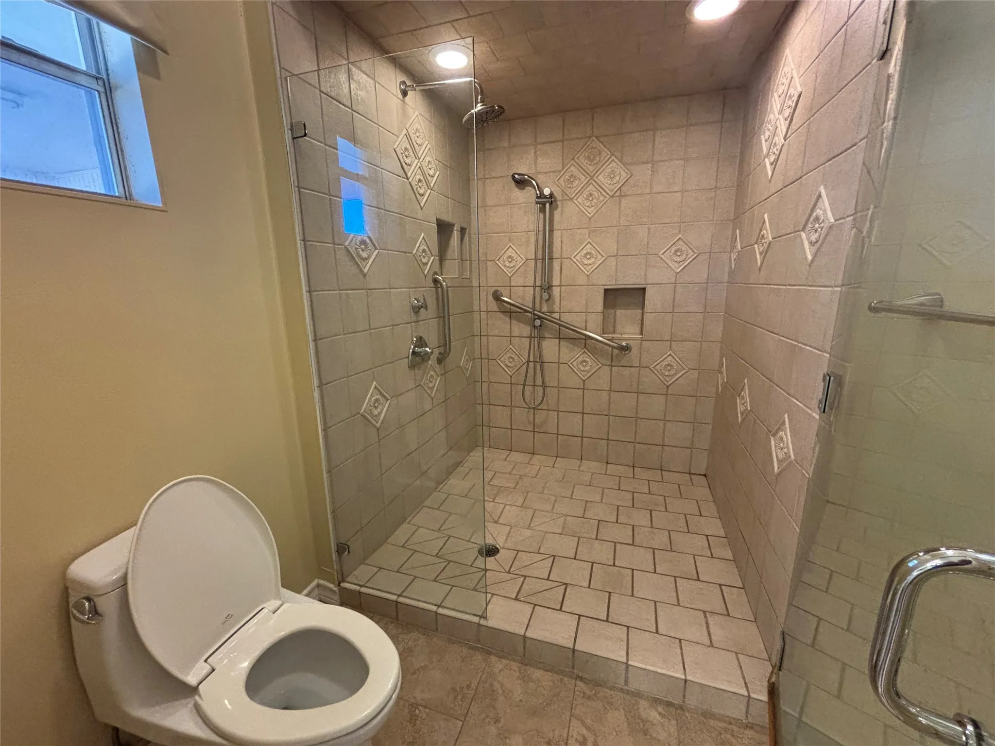 Tiled walk-in shower with glass enclosure, built-in shelf, grab bars, and rain shower head