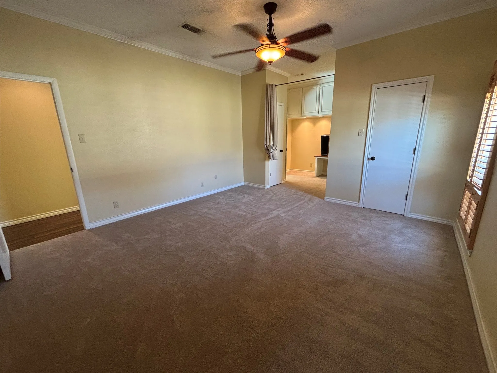 Spacious room featuring carpet flooring, crown molding, a ceiling fan with integrated lighting, and a separate alcove with built-in cabinetry