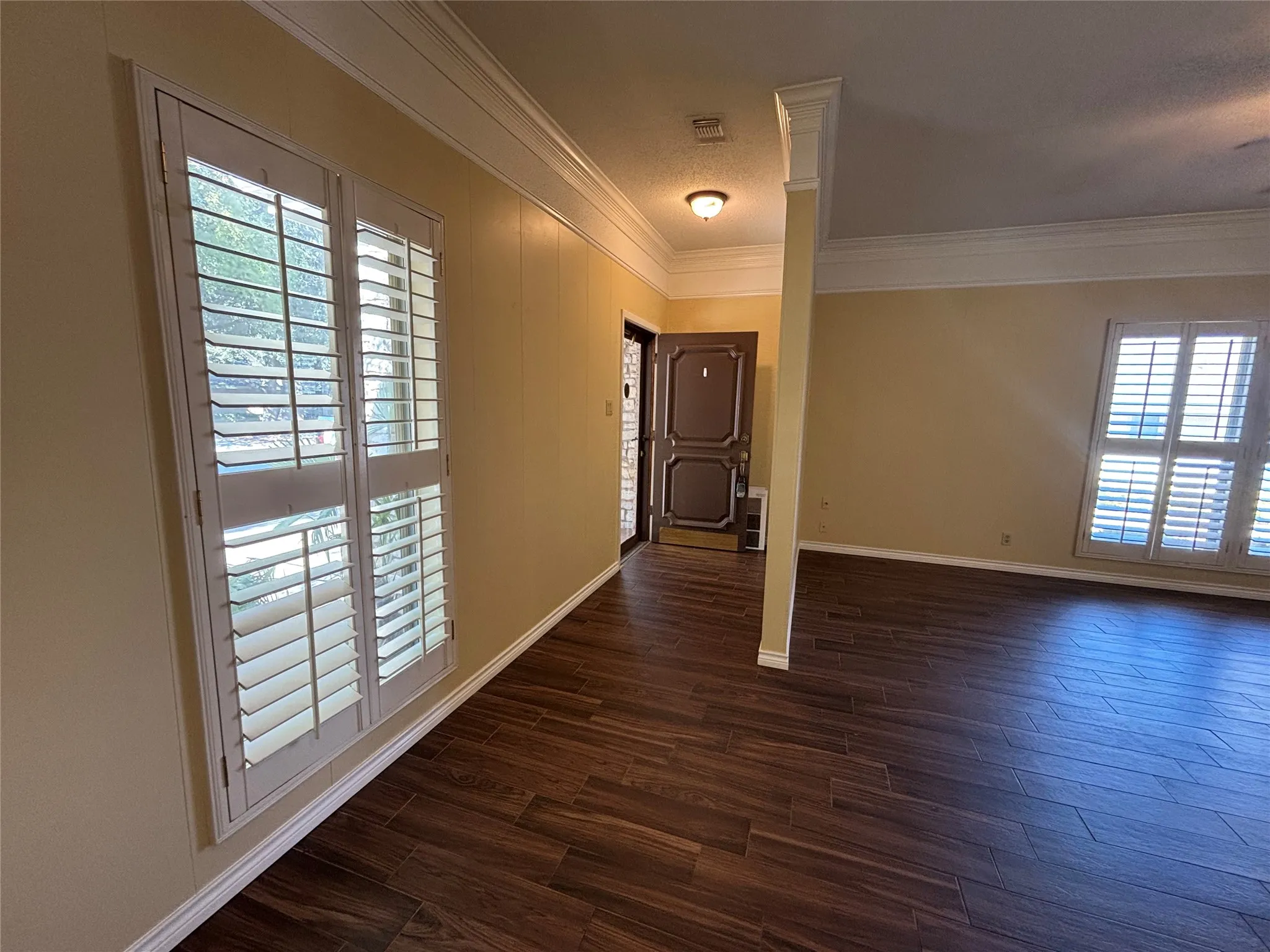 Wood-finish flooring throughout, crown molding, plantation shutters, and a paneled entry door