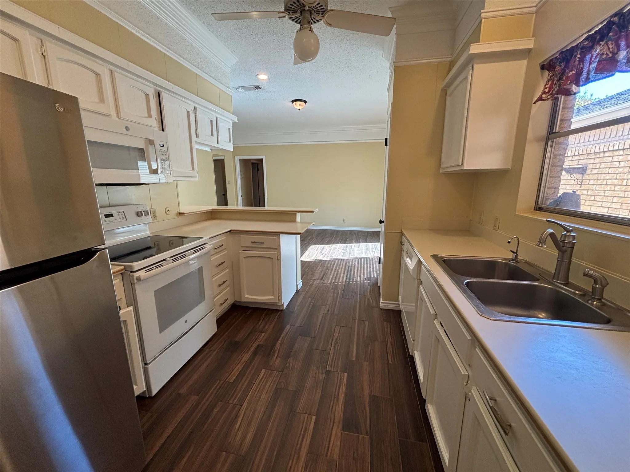 Kitchen featuring white cabinetry, stainless steel refrigerator, built-in microwave, and wood-finish flooring