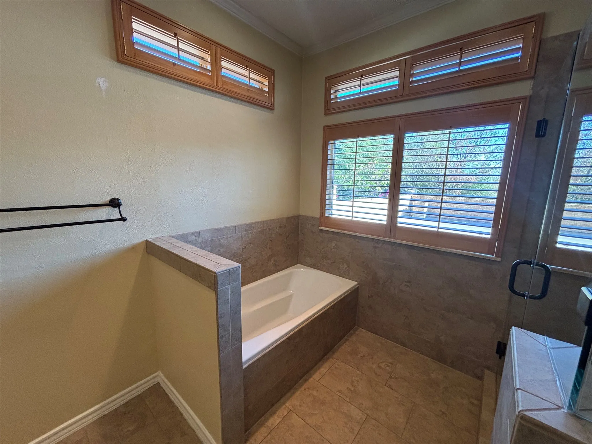 Soaking tub with surrounding tile, wood-finish window shutters, and tiled flooring