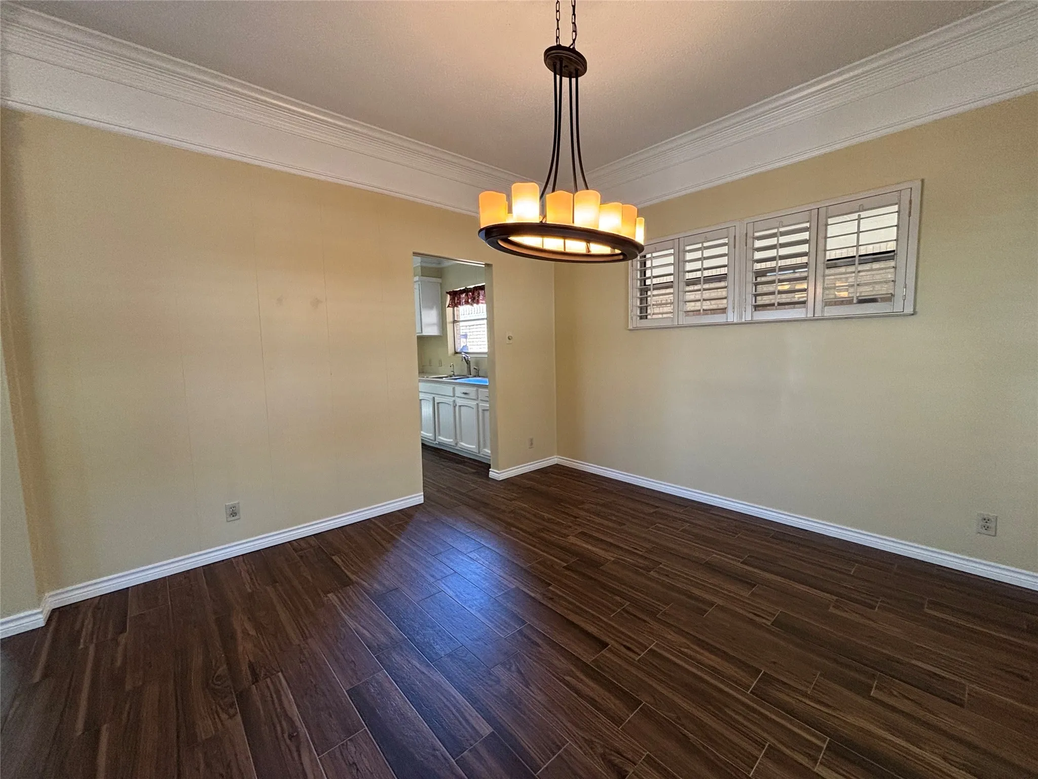 Dark wood-finish flooring, crown molding, and a chandelier with a bronze-finish frame