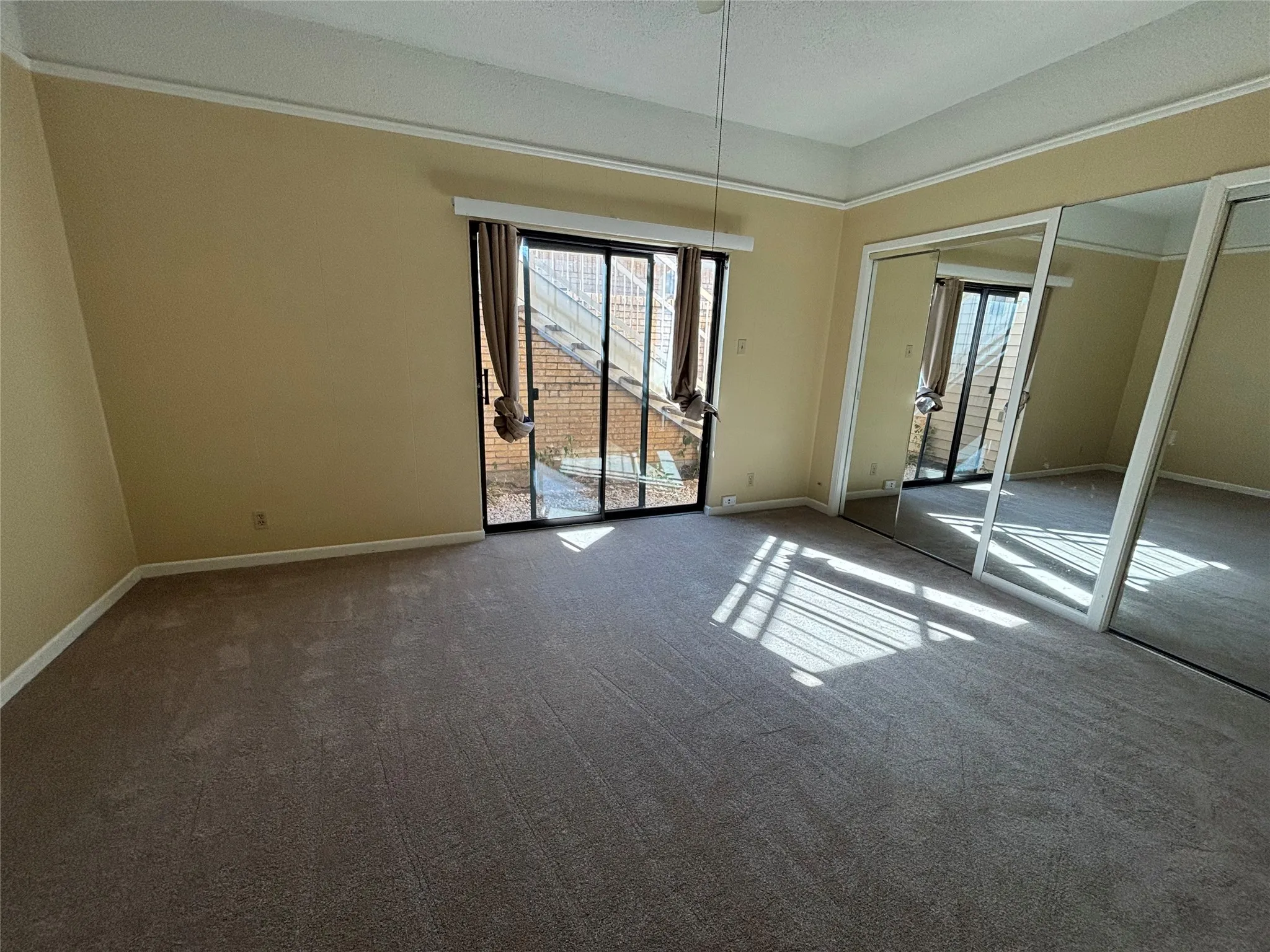 Carpeted flooring, mirrored sliding closet doors, sliding glass door, crown molding, and painted walls