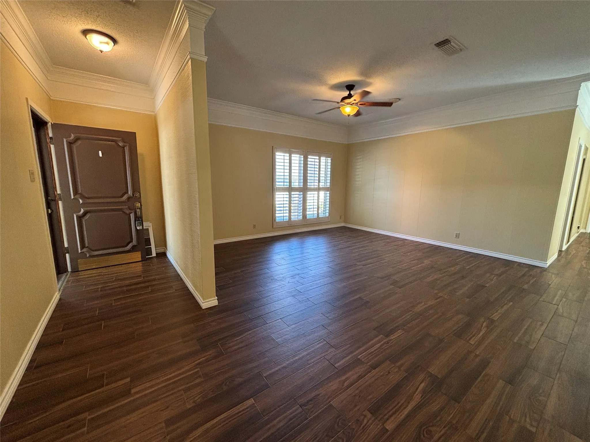 Wood-look tile flooring throughout, crown molding, ceiling fan, and window with plantation shutters