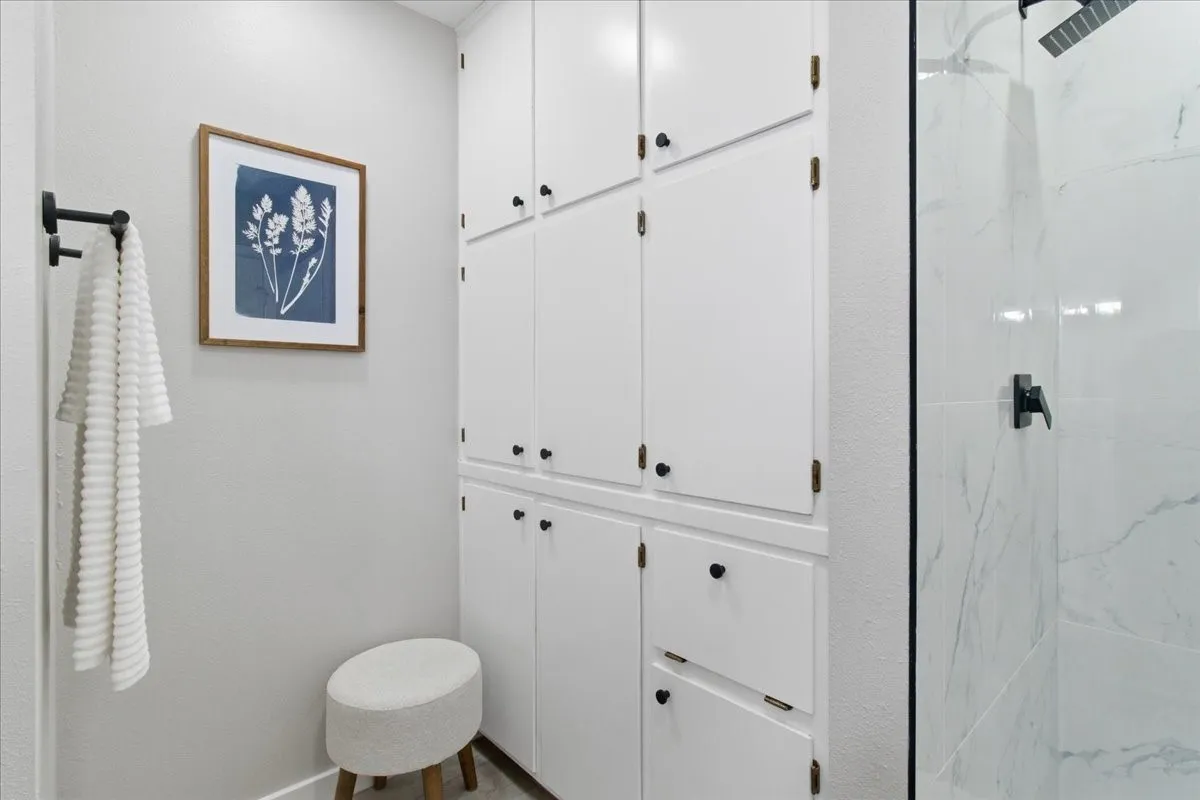 Built-in white cabinetry with matte black hardware, glass-enclosed shower with white tiled walls, and a matte black shower head