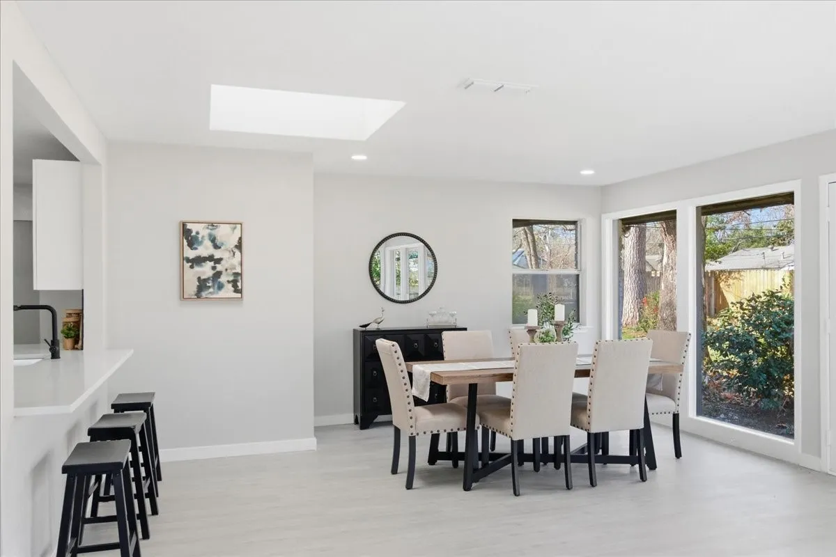 Spacious dining area with light wood-finish flooring, a skylight, and large windows