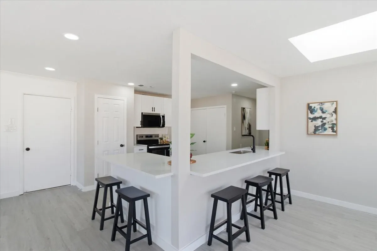 Kitchen peninsula with white countertop and integrated sink, black wall-mounted faucet, recessed lighting, and a skylight