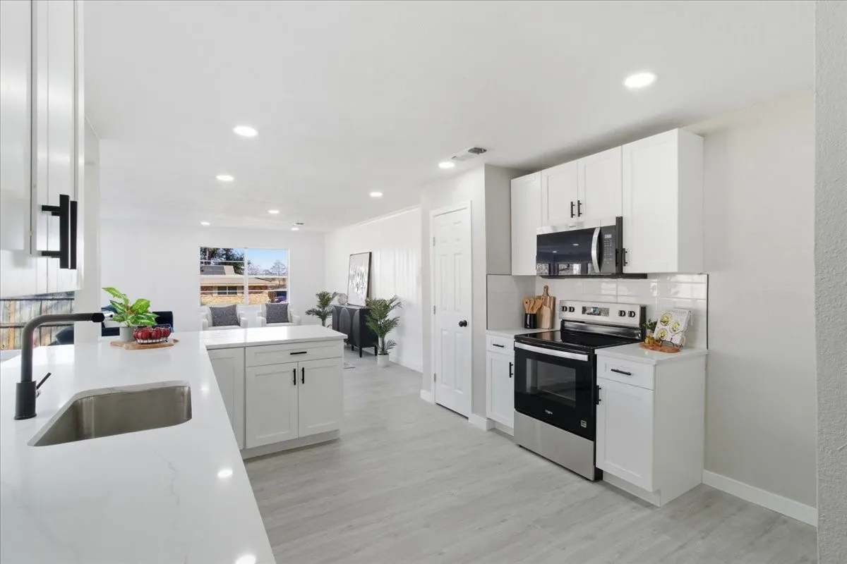 White shaker cabinetry with black hardware, stainless steel appliances, recessed lighting, wood-finish flooring, and a subway tile backsplash