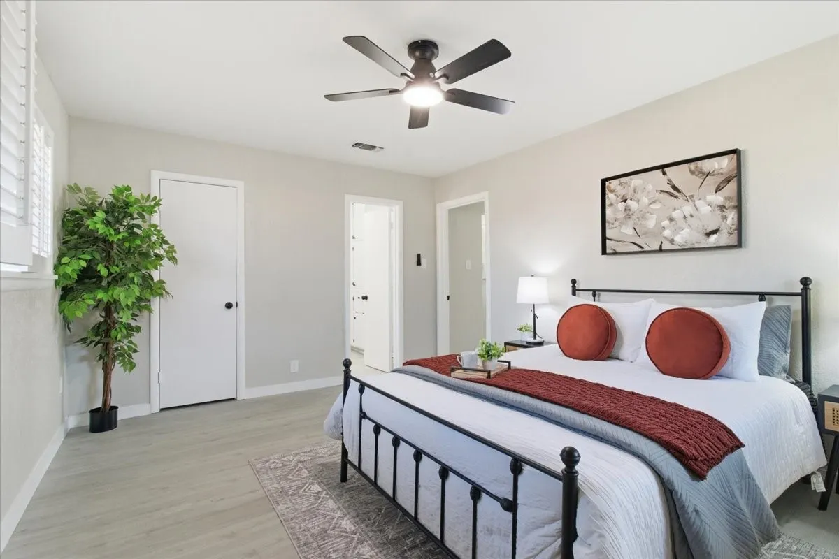 Light-toned wood-finish flooring, white interior doors, window with plantation shutters, and a ceiling fan