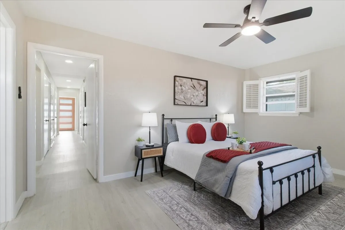 Light wood-finish flooring, a contemporary ceiling fan with integrated lighting, and a window with plantation shutters