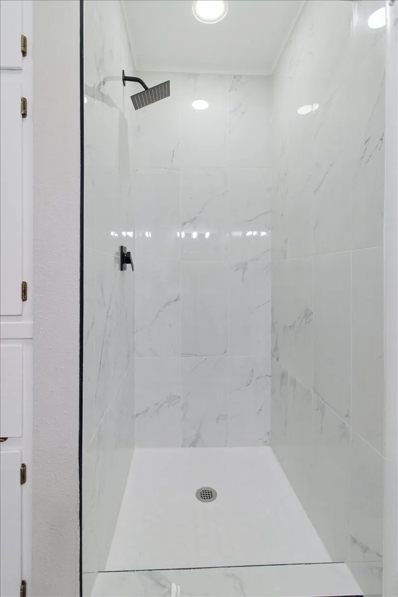 Walk-in shower with white tile surround, black finish shower fixtures, glass enclosure, and recessed lighting