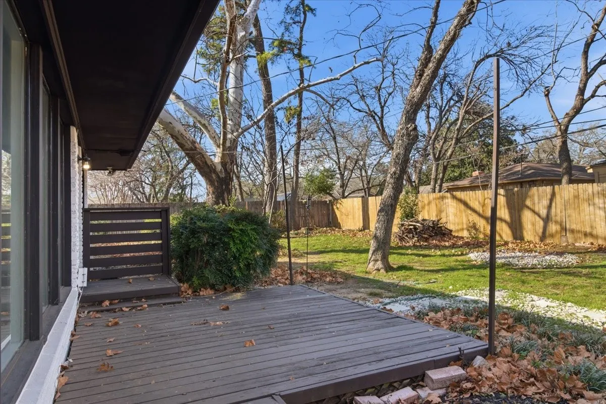 Expansive yard featuring a wooden privacy fence, mature trees, and a ground-level wood deck