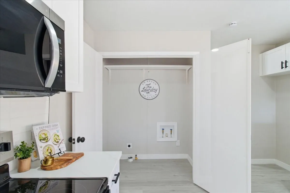 White cabinetry, built-in microwave, light-toned flooring, and laundry closet with utility hookups