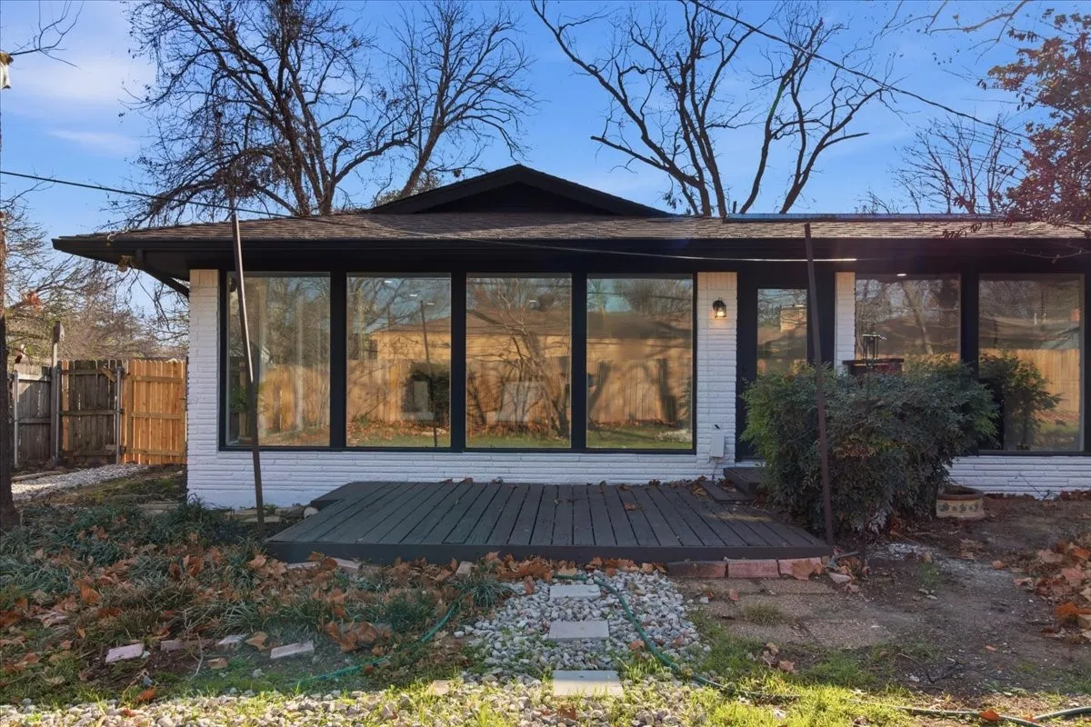 White brick exterior with black trim, expansive picture windows, dark wood-finish decking, and a contemporary exterior light fixture