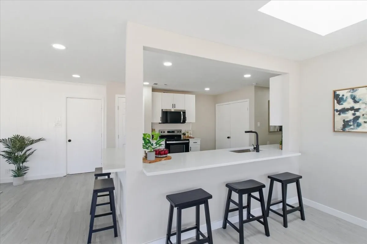 Kitchen featuring a pass-through counter with seating, white cabinetry, black appliances, a single-basin sink with a matte black faucet, and recessed lighting