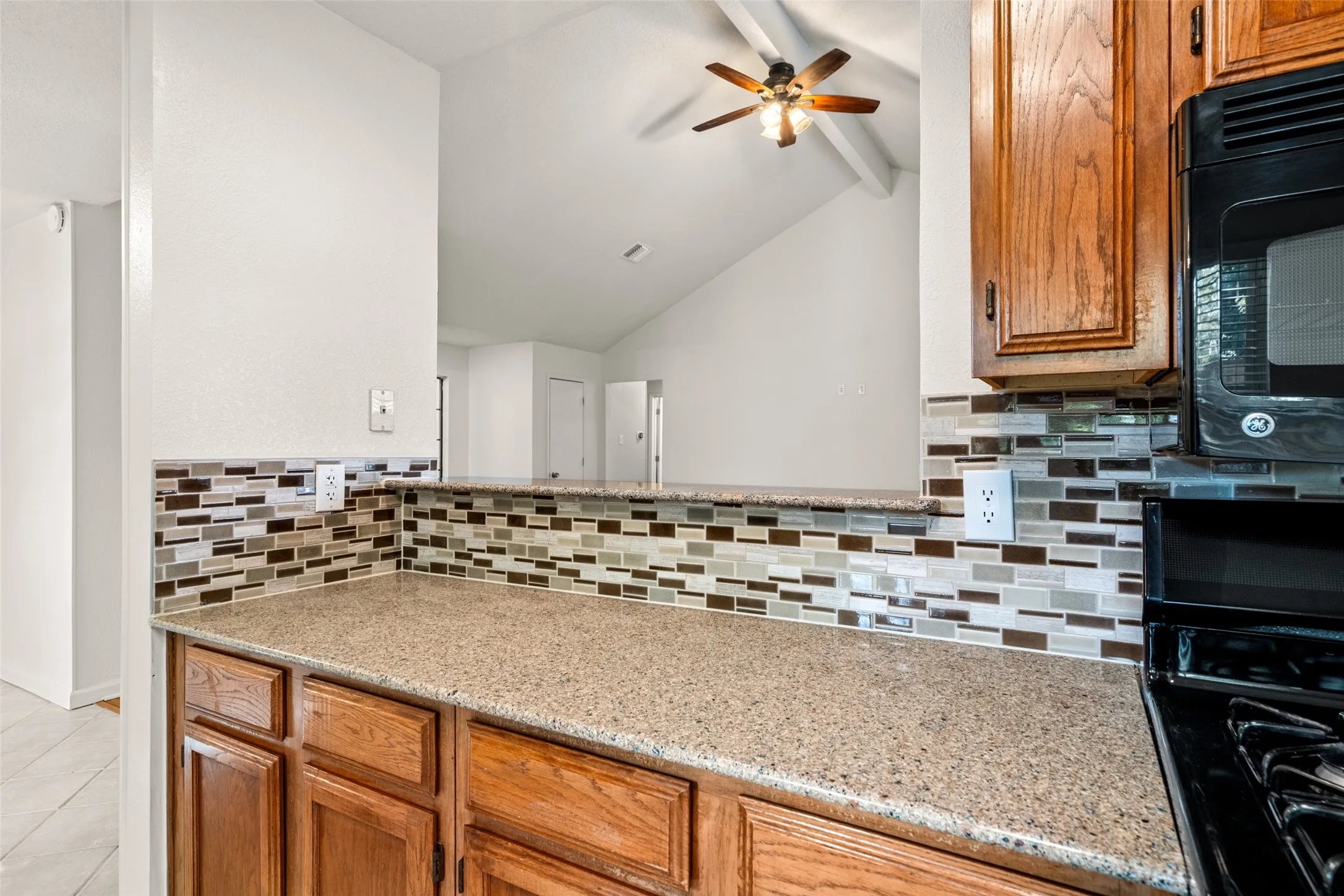 Granite-finish countertops, mosaic tile backsplash, wood cabinetry, vaulted ceiling, and ceiling fan