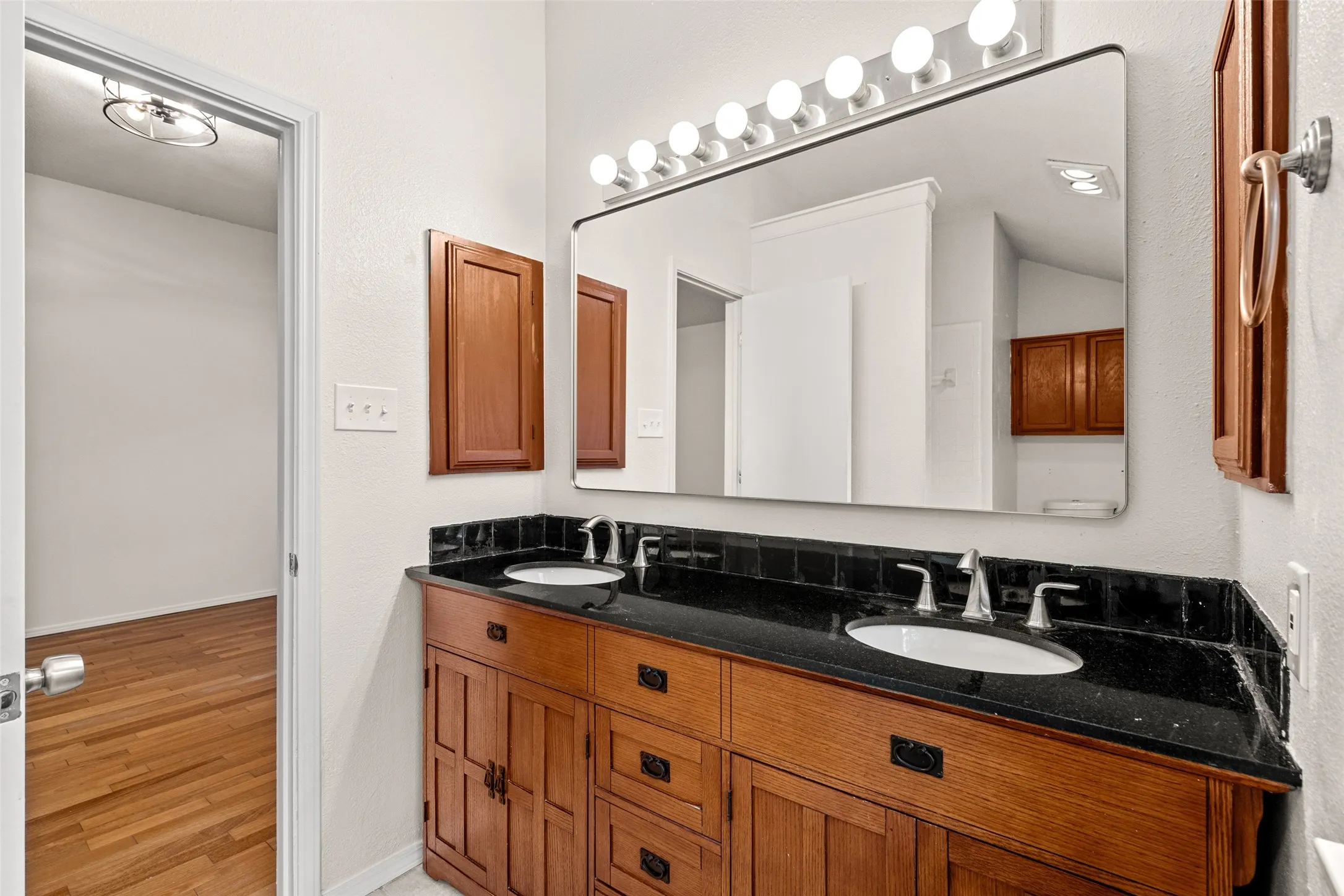 Double vanity with dark stone countertop, dual undermount sinks, and wood cabinetry