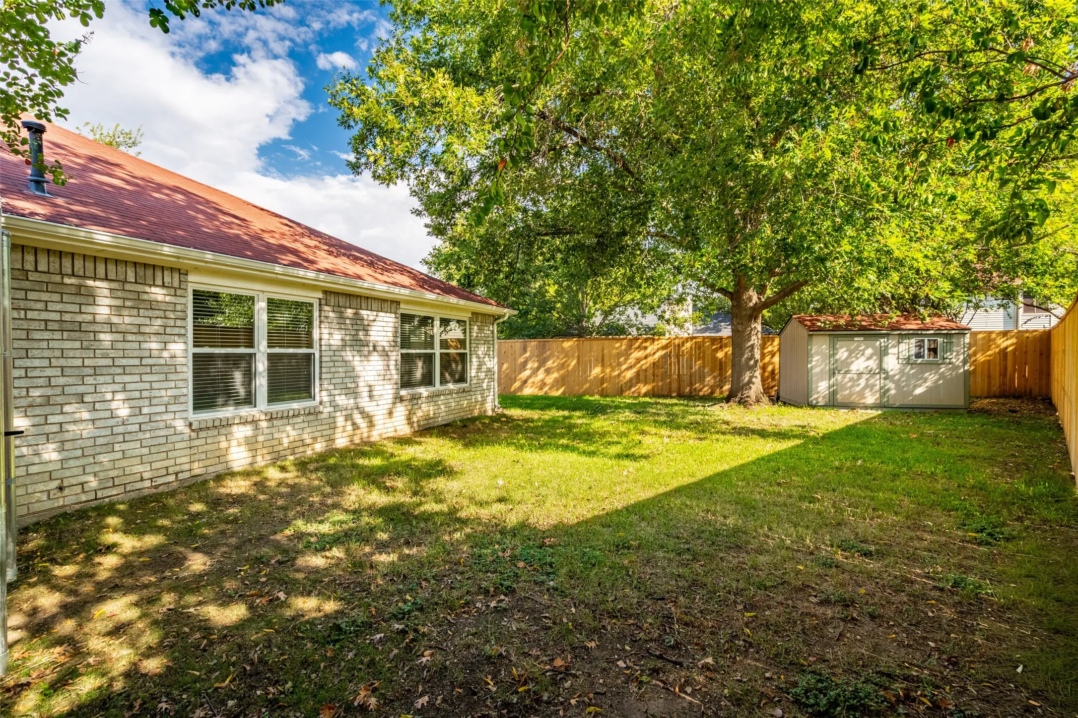 Fenced backyard featuring a storage shed, established trees, and a brick exterior with multiple windows