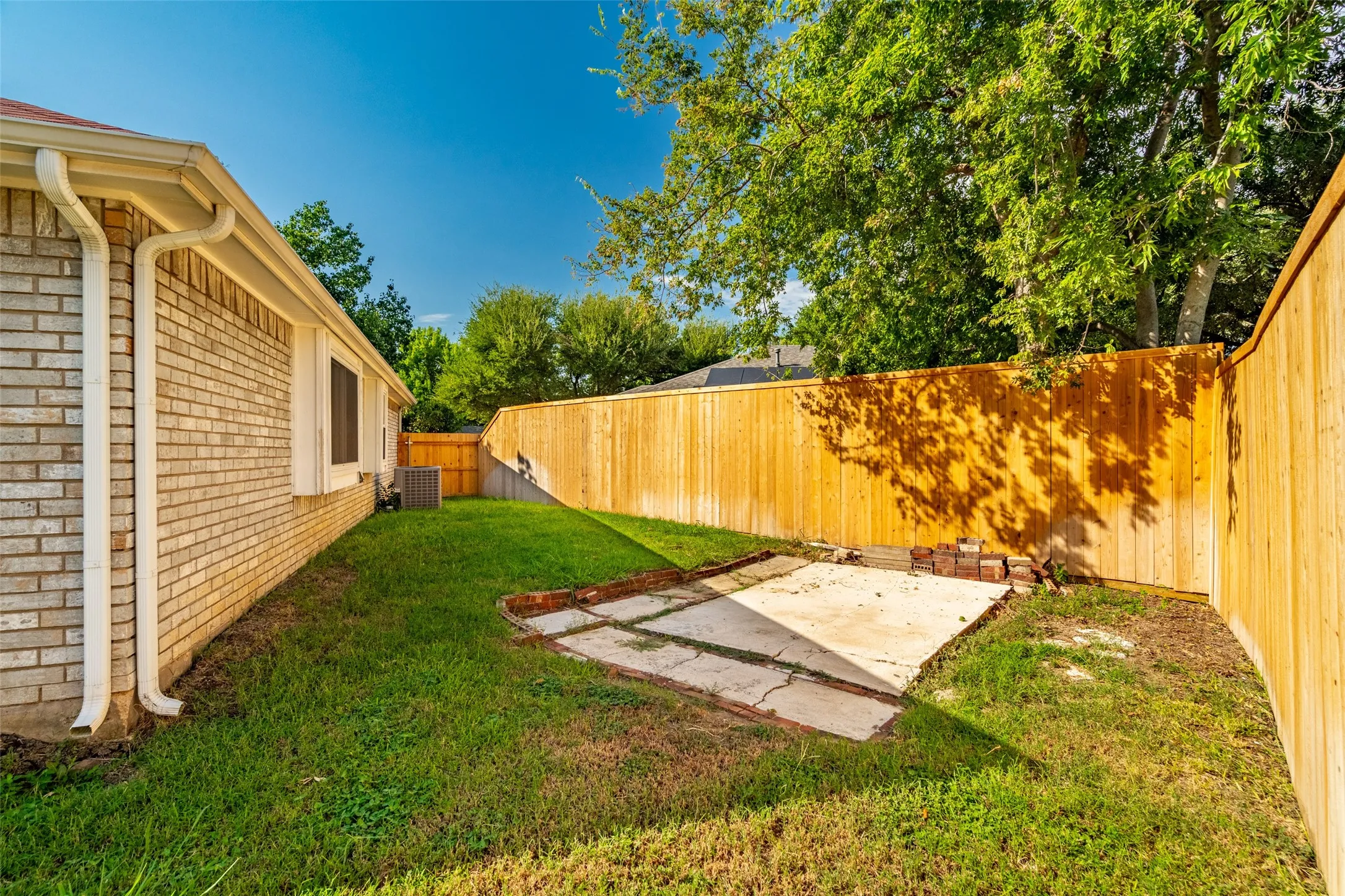Lawn area with a partial concrete patio, surrounded by a wood privacy fence