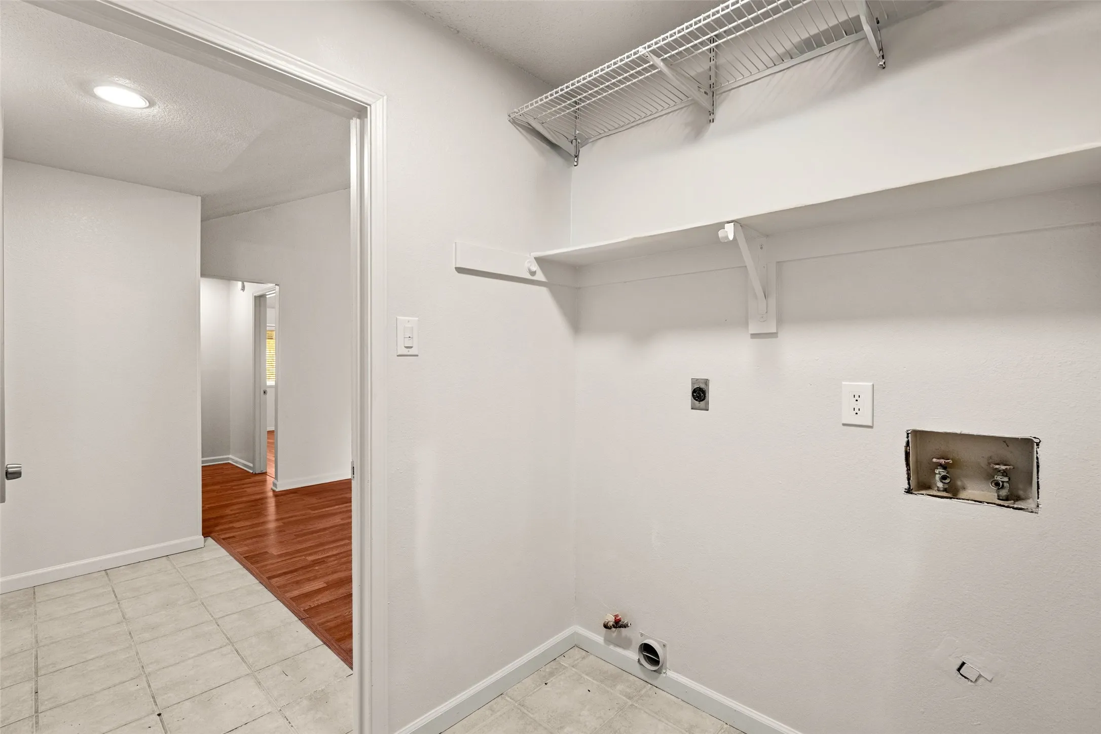 Laundry area with tile flooring, built-in shelving, and utility hookups