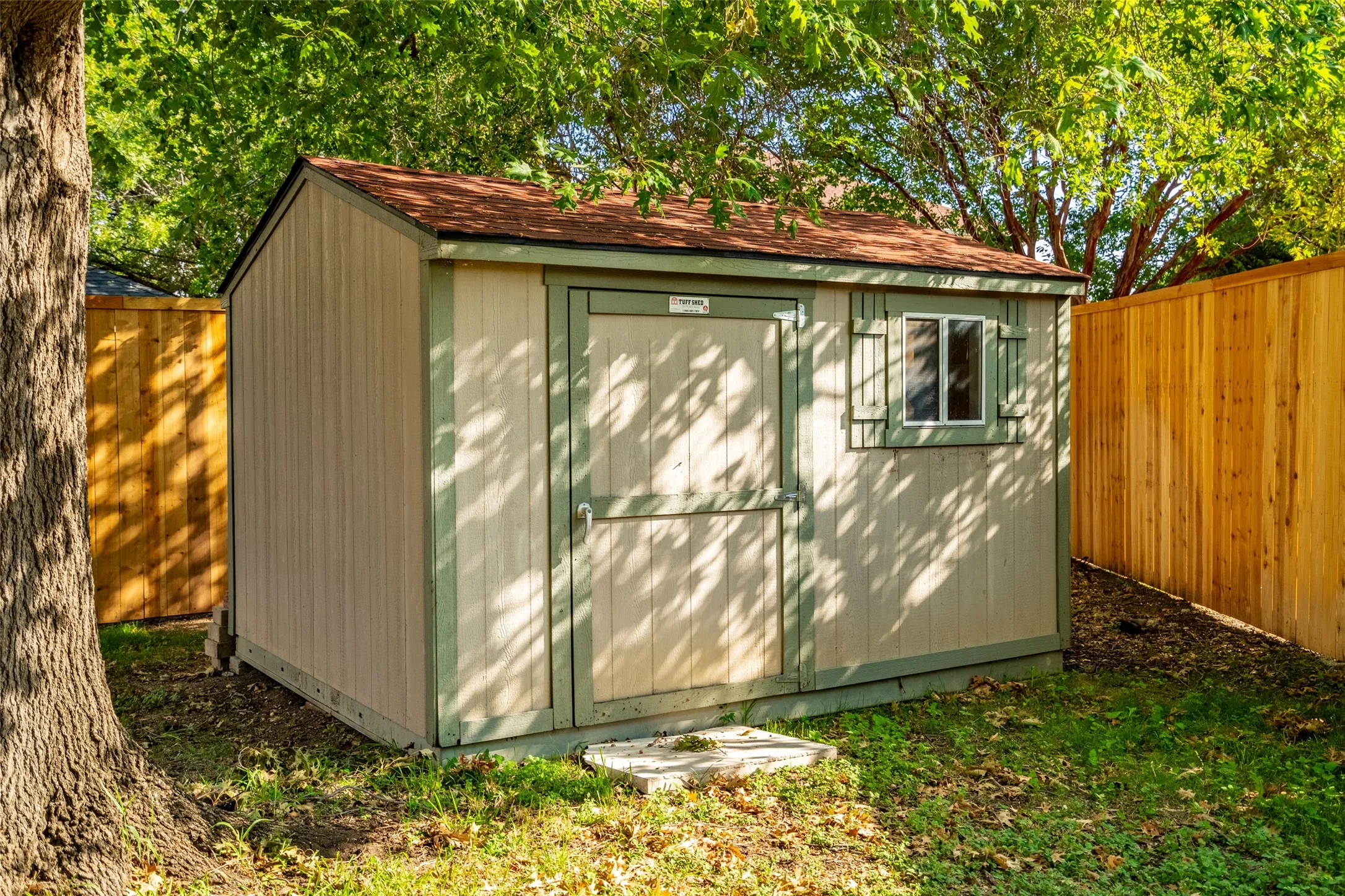 Storage shed with a red-shingle roof, wood siding, and a single window with shutters