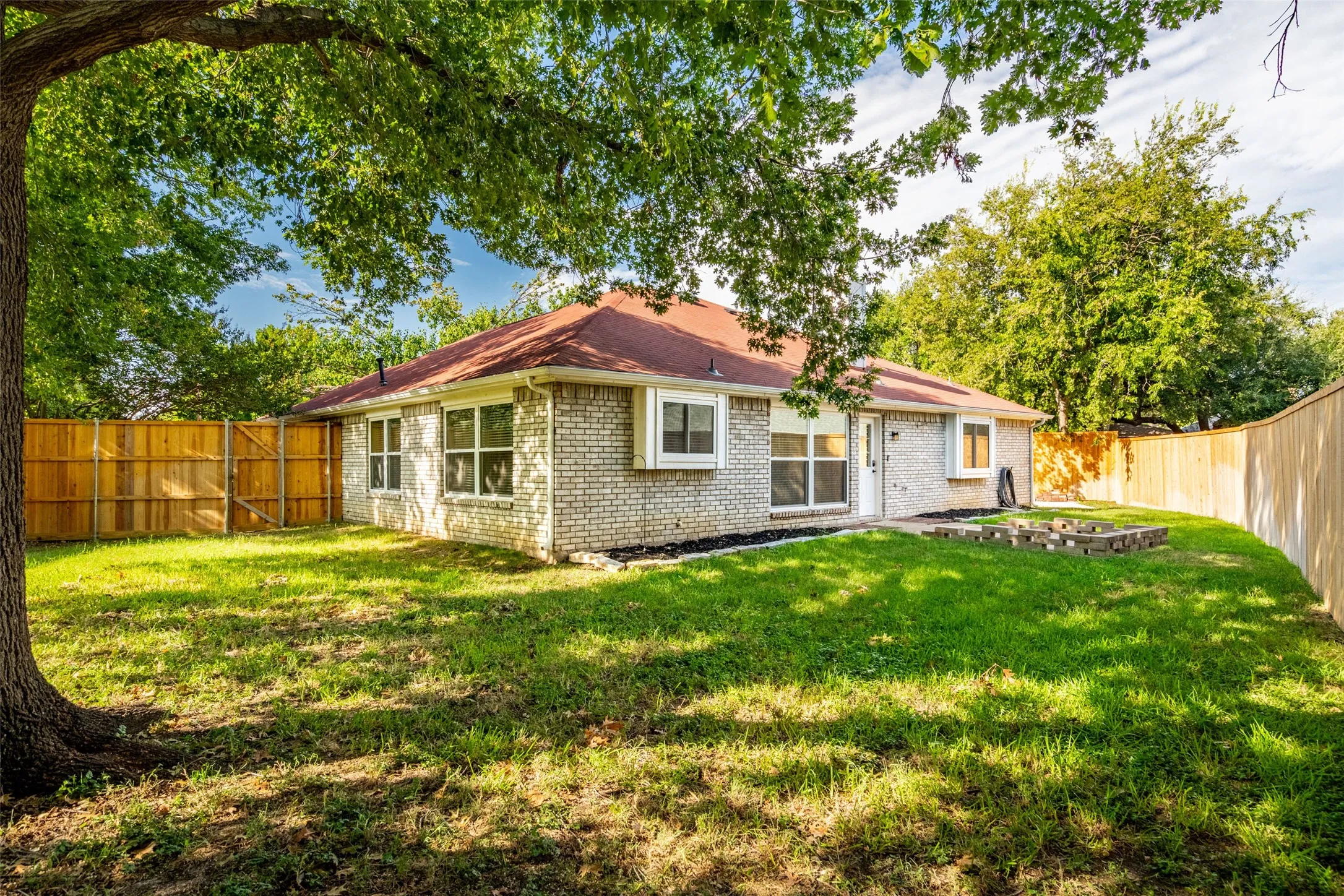 Expansive backyard with a manicured lawn, full privacy fencing, and a red shingle roof