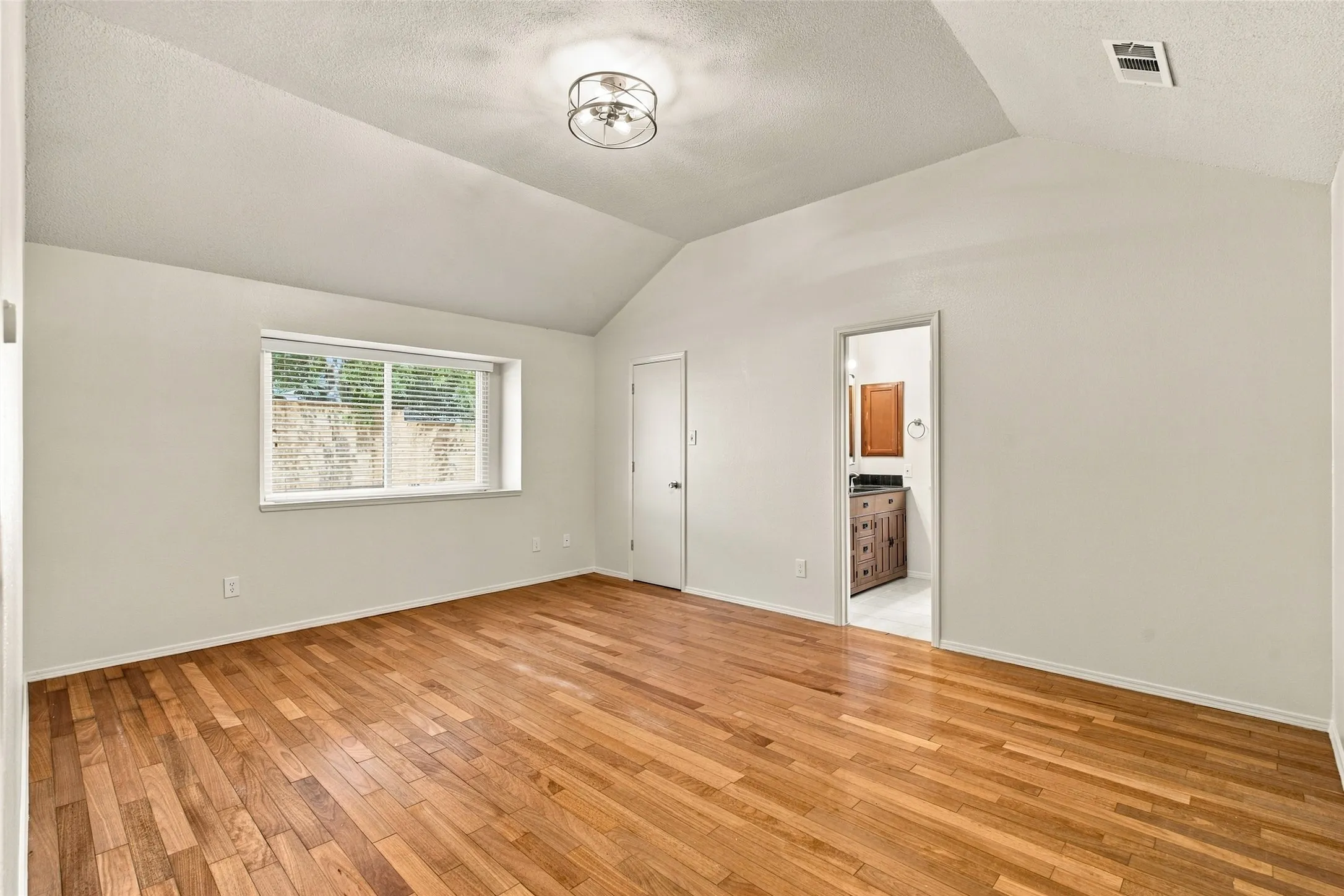 Vaulted ceiling, wood-finish flooring, flush mount ceiling light, and window with blinds