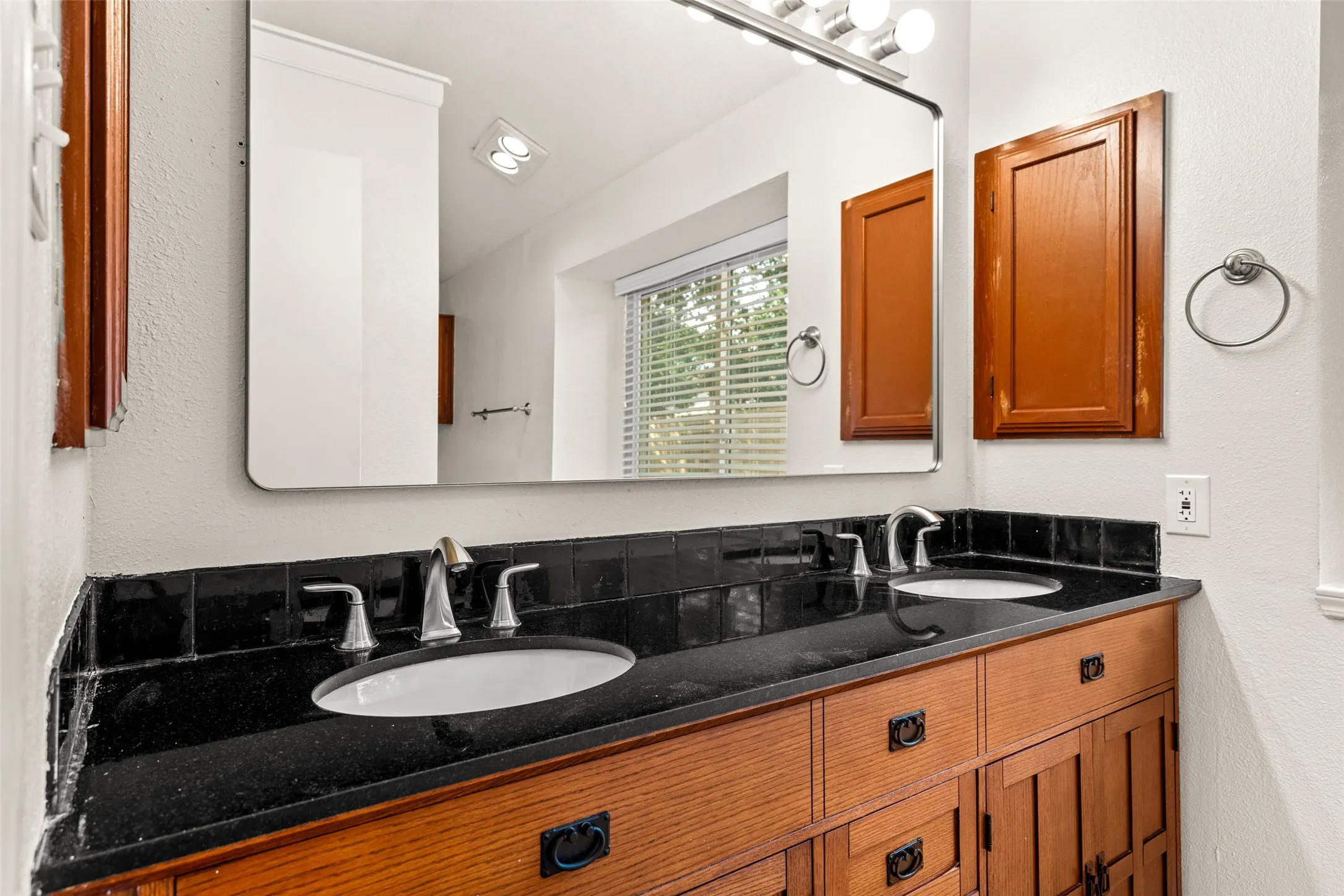 Dual vanity with a dark stone countertop, integrated sinks, and wood-finish cabinetry