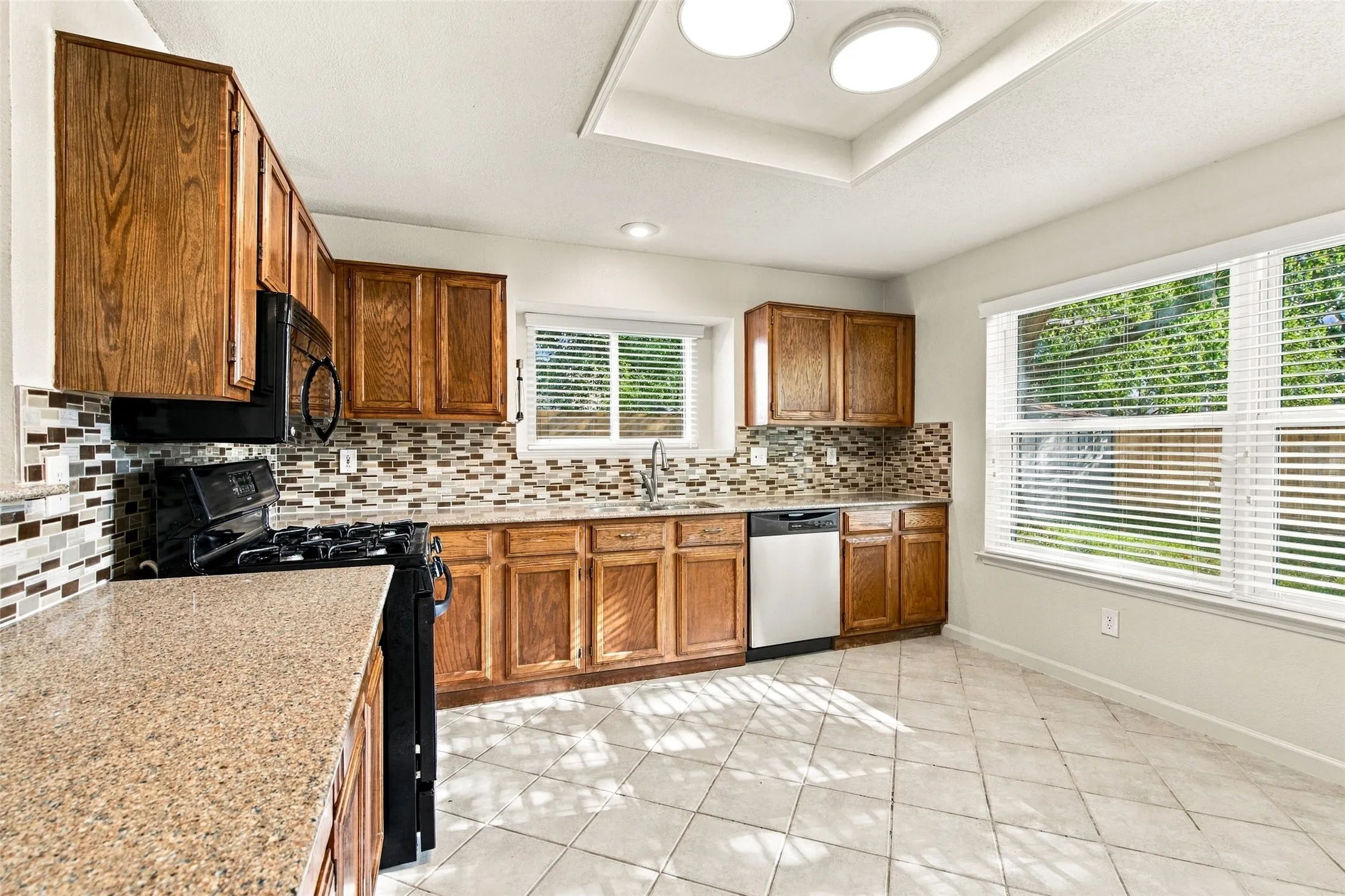 Kitchen featuring wood cabinetry, a tiled backsplash, granite-finish countertops, stainless steel appliances, and tiled flooring