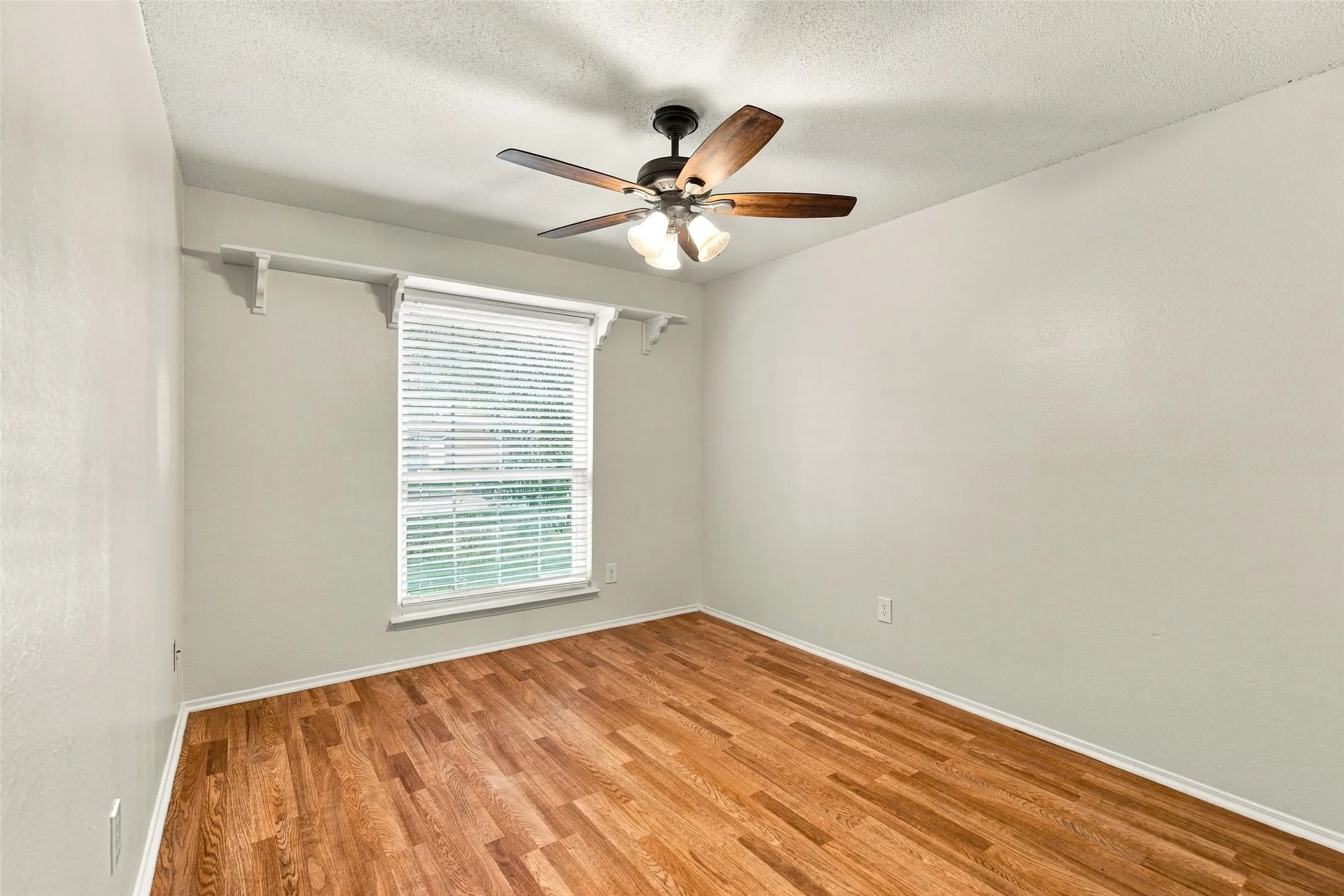 Wood-finish flooring, ceiling fan with integrated lighting, window with blinds, and light-toned walls