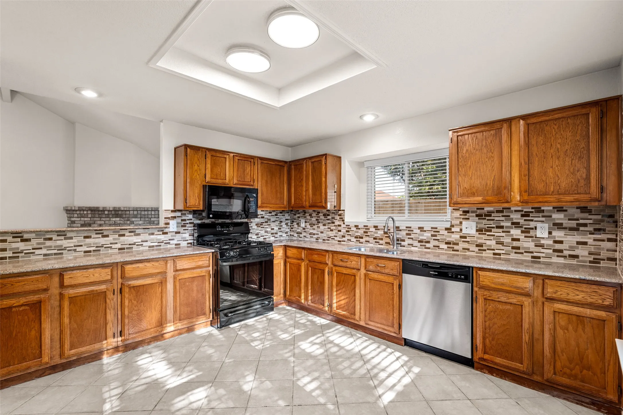 Kitchen featuring wood cabinetry, built-in black appliances, mosaic tile backsplash, and a stainless steel dishwasher