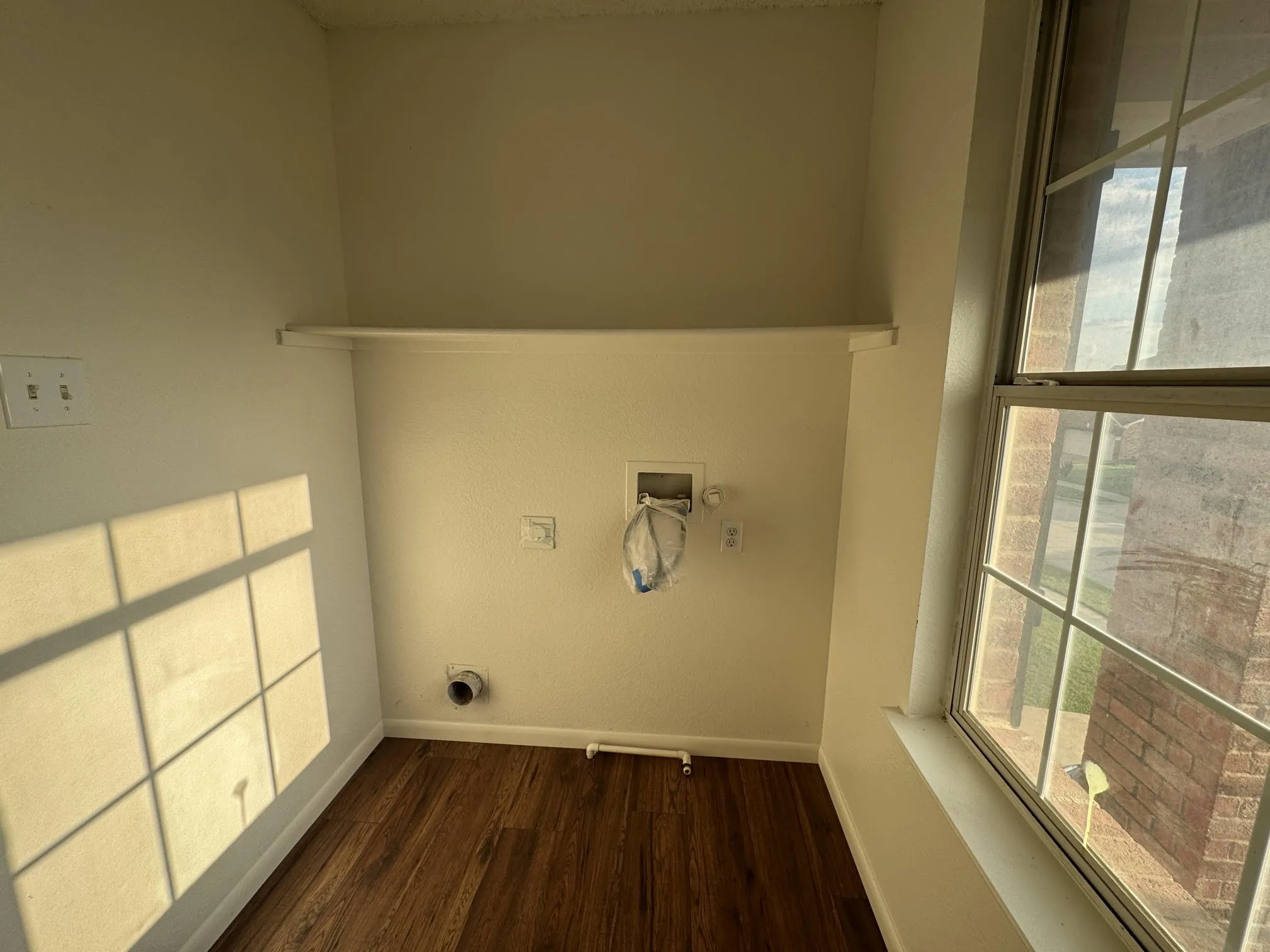 Dedicated utility space featuring wood-finish flooring, a functional window with grid panes, and a convenient upper shelf