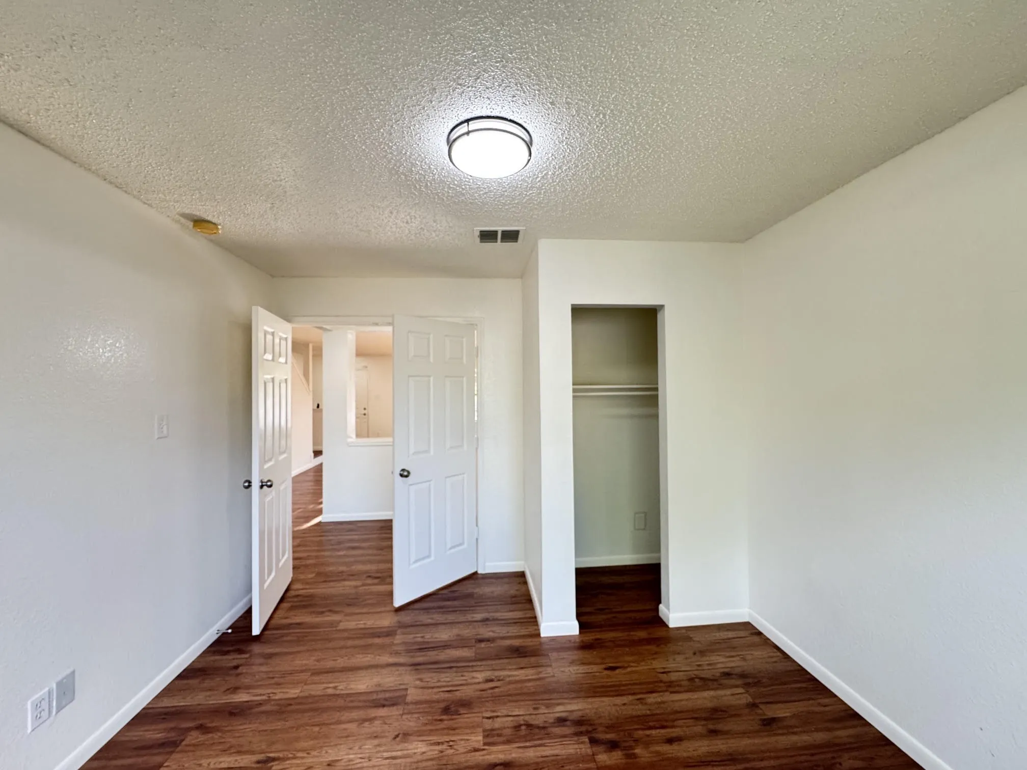 Interior room featuring wood-finish flooring, white walls, and a recessed closet with a clothes rod