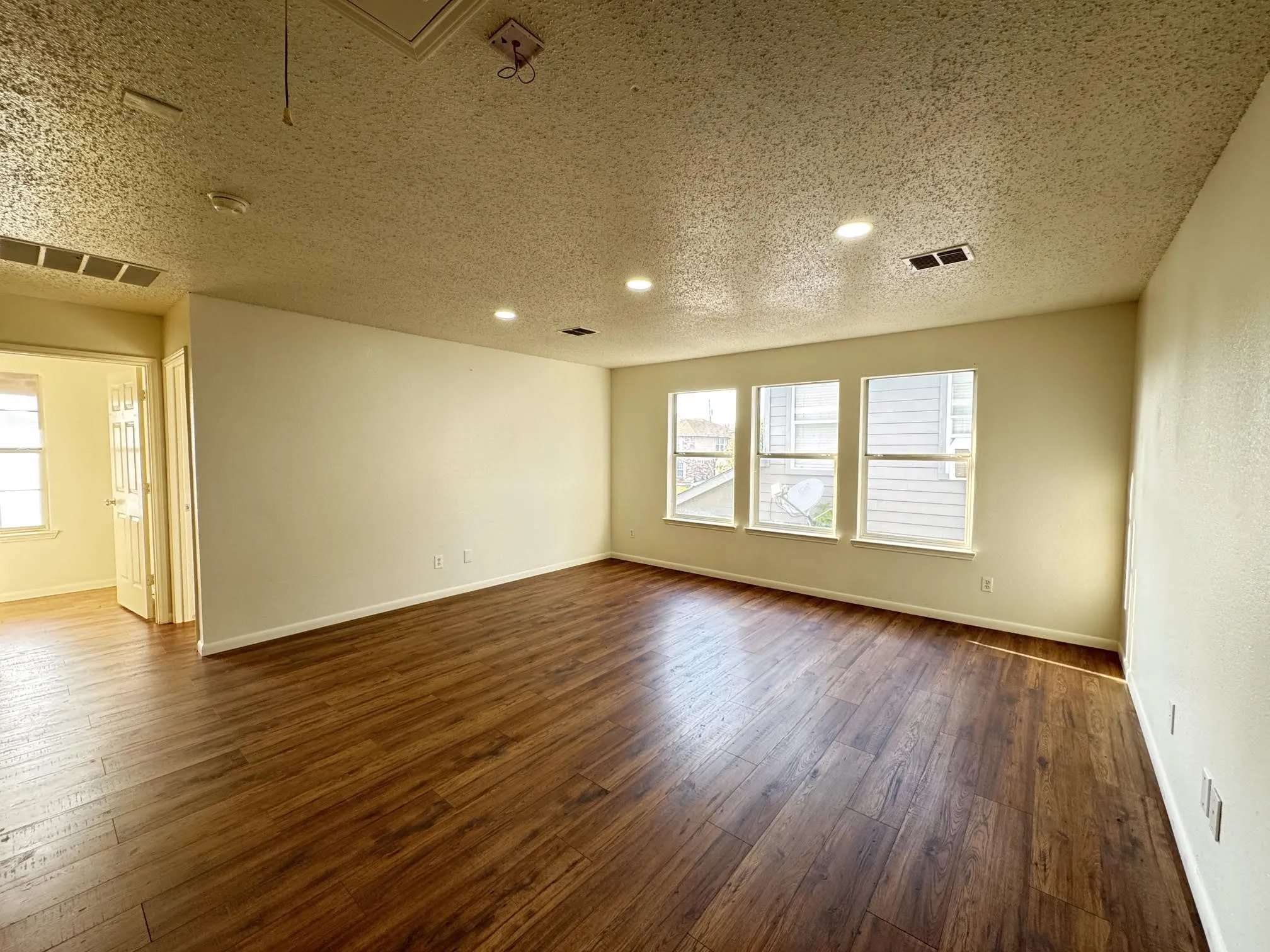 Spacious room featuring wood-finish flooring, recessed lighting, and three large windows