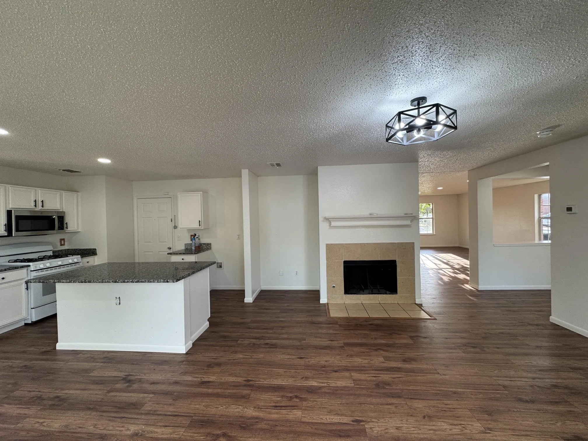 Open-concept living space with wood-finish flooring, a central kitchen island, and a fireplace with a tile surround
