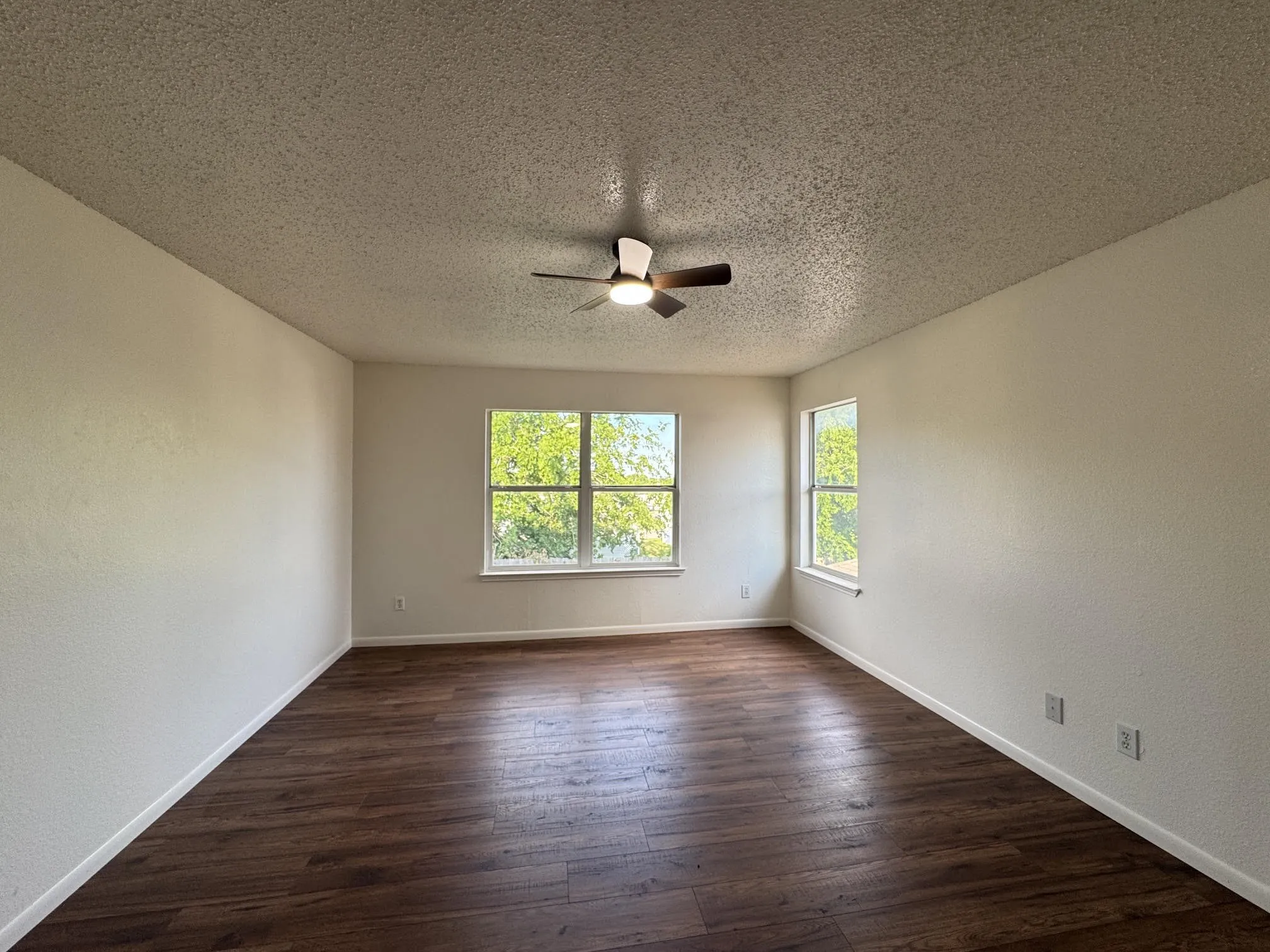 Spacious room featuring wood-finish flooring, light-toned walls, and multiple windows
