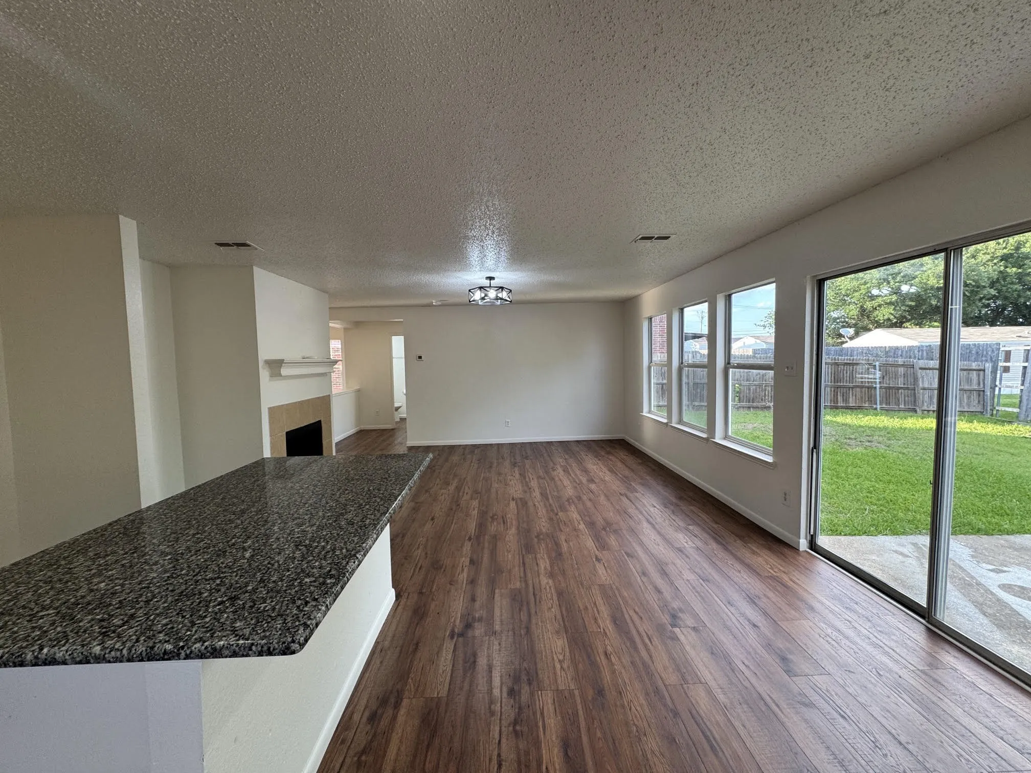 Spacious interior featuring wood-finish flooring, a contemporary ceiling light fixture, and a breakfast bar with a speckled countertop