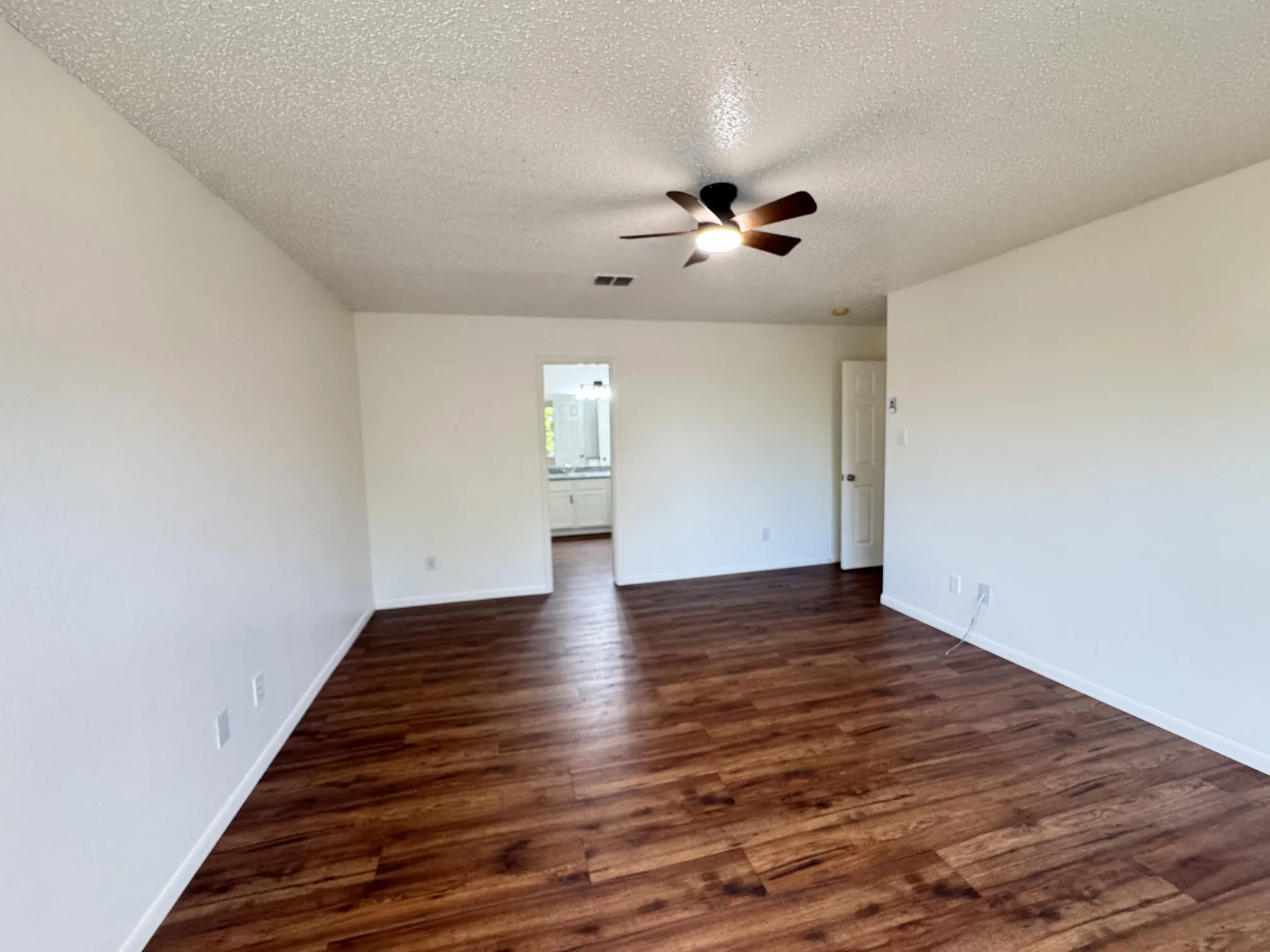 Spacious room featuring wood-finish flooring, light-colored walls, and a ceiling fan