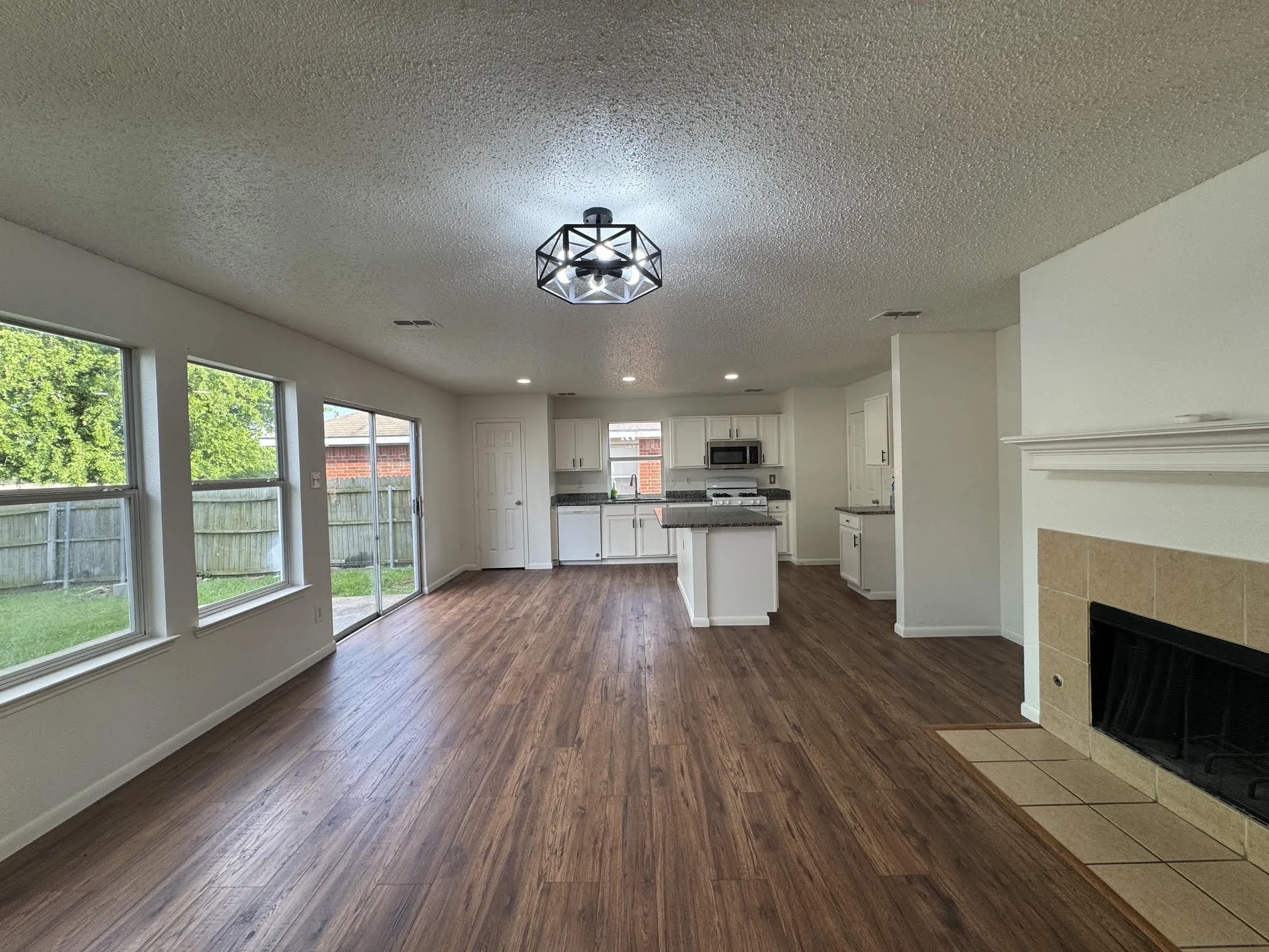 Spacious open-concept living area featuring wood-finish flooring, a contemporary ceiling light fixture, and large windows