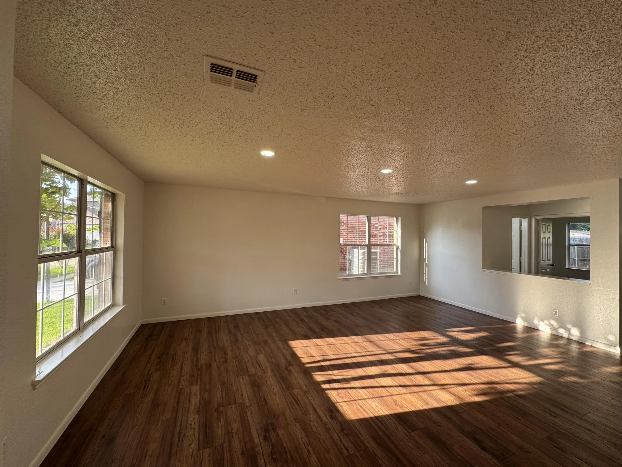 Spacious interior room featuring wood-finish flooring, two large windows, and a pass-through opening