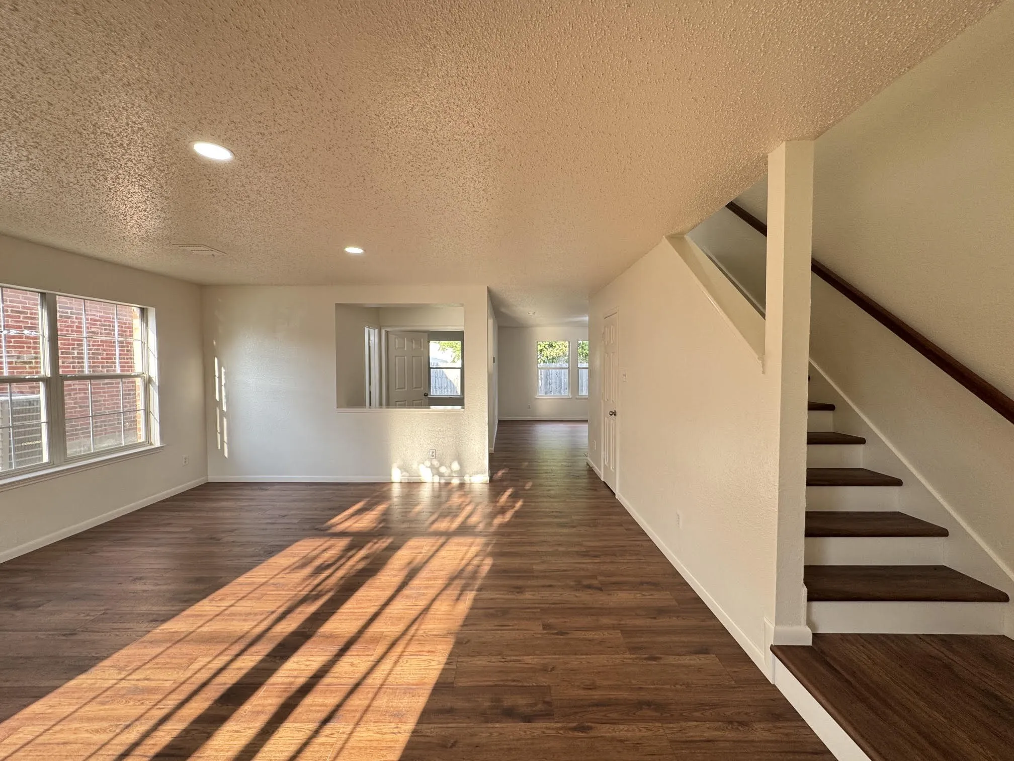 Open-concept living area featuring wood-finish flooring, recessed lighting, and a prominent staircase with wood treads and handrail