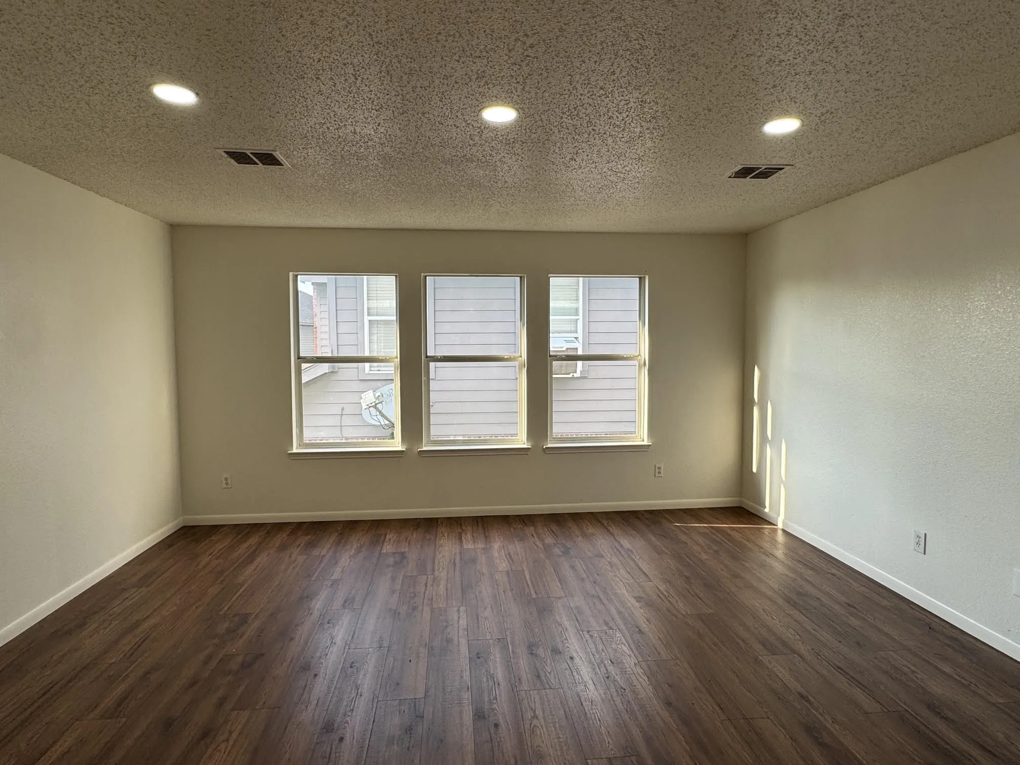 Bright interior space featuring three windows, recessed ceiling lighting, wood-finish flooring, and crisp white walls