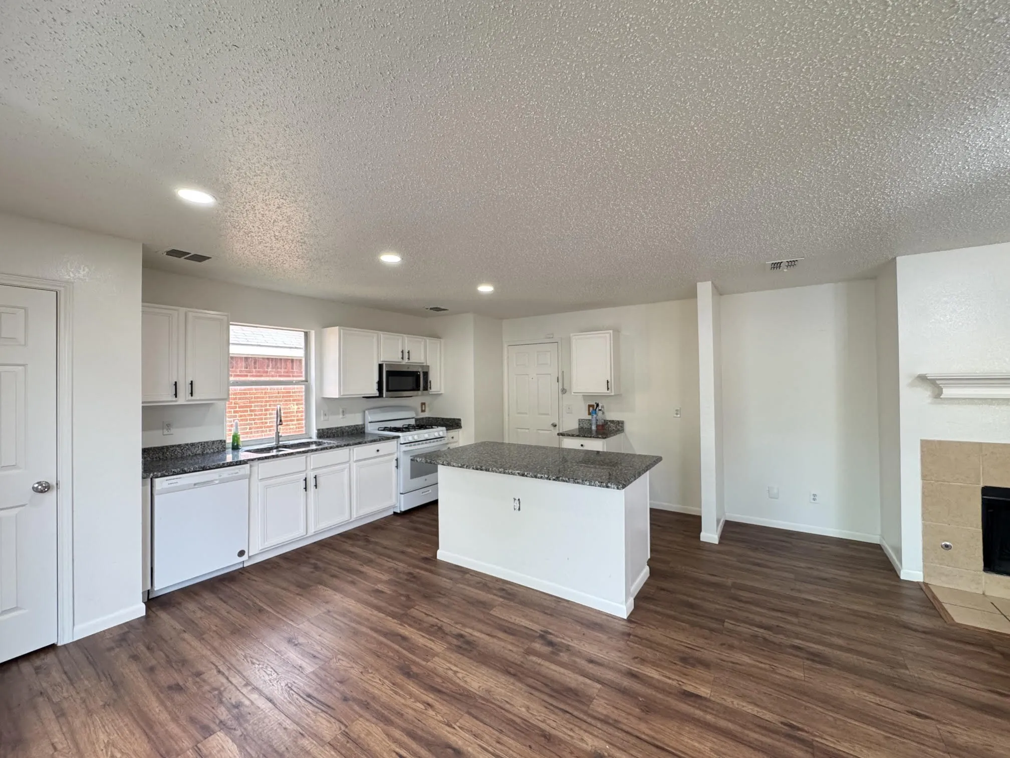Open-concept kitchen featuring white cabinetry, dark speckled countertops, and a central island